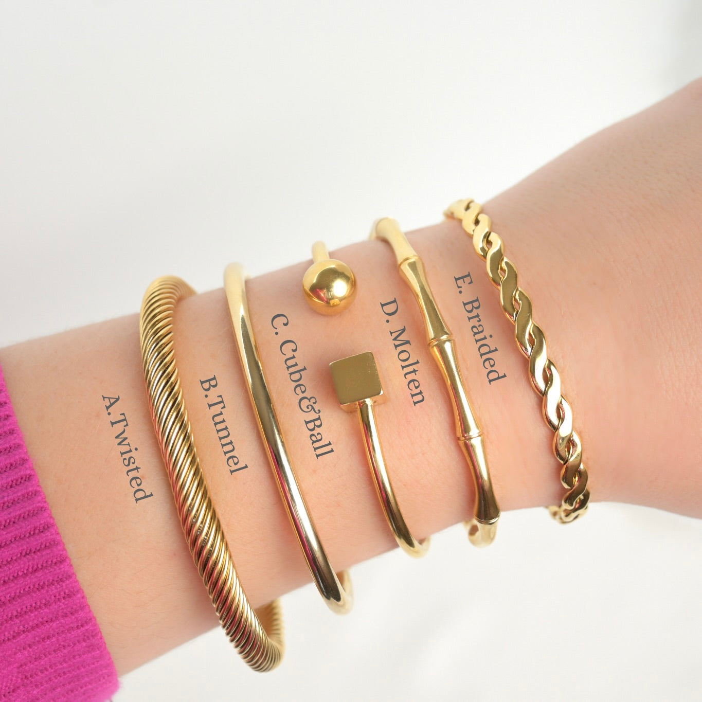 Gold cuff bracelets on a wrist with labels on a white background