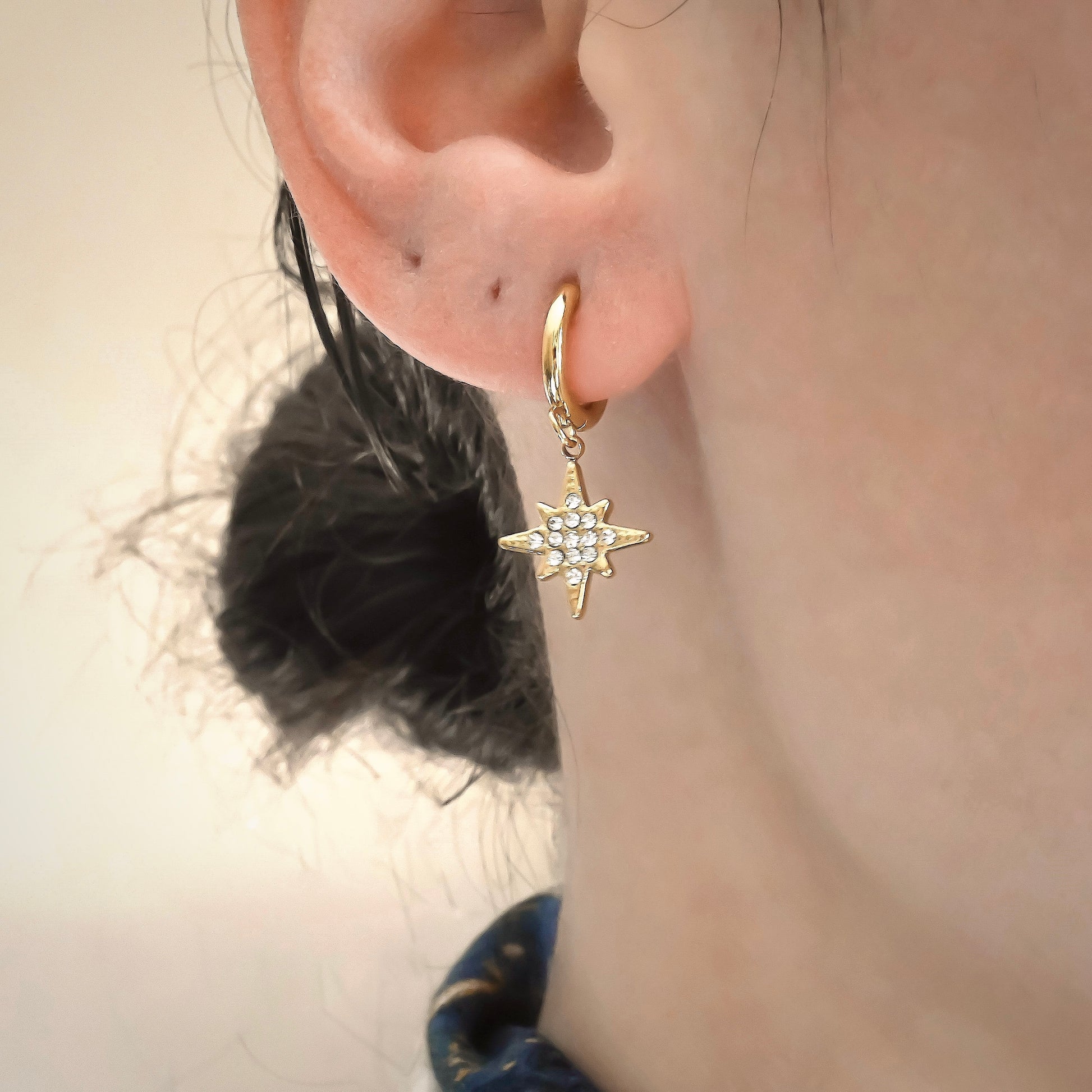 Gold star charm earrings with pave diamonds worn by a person with a neutral background