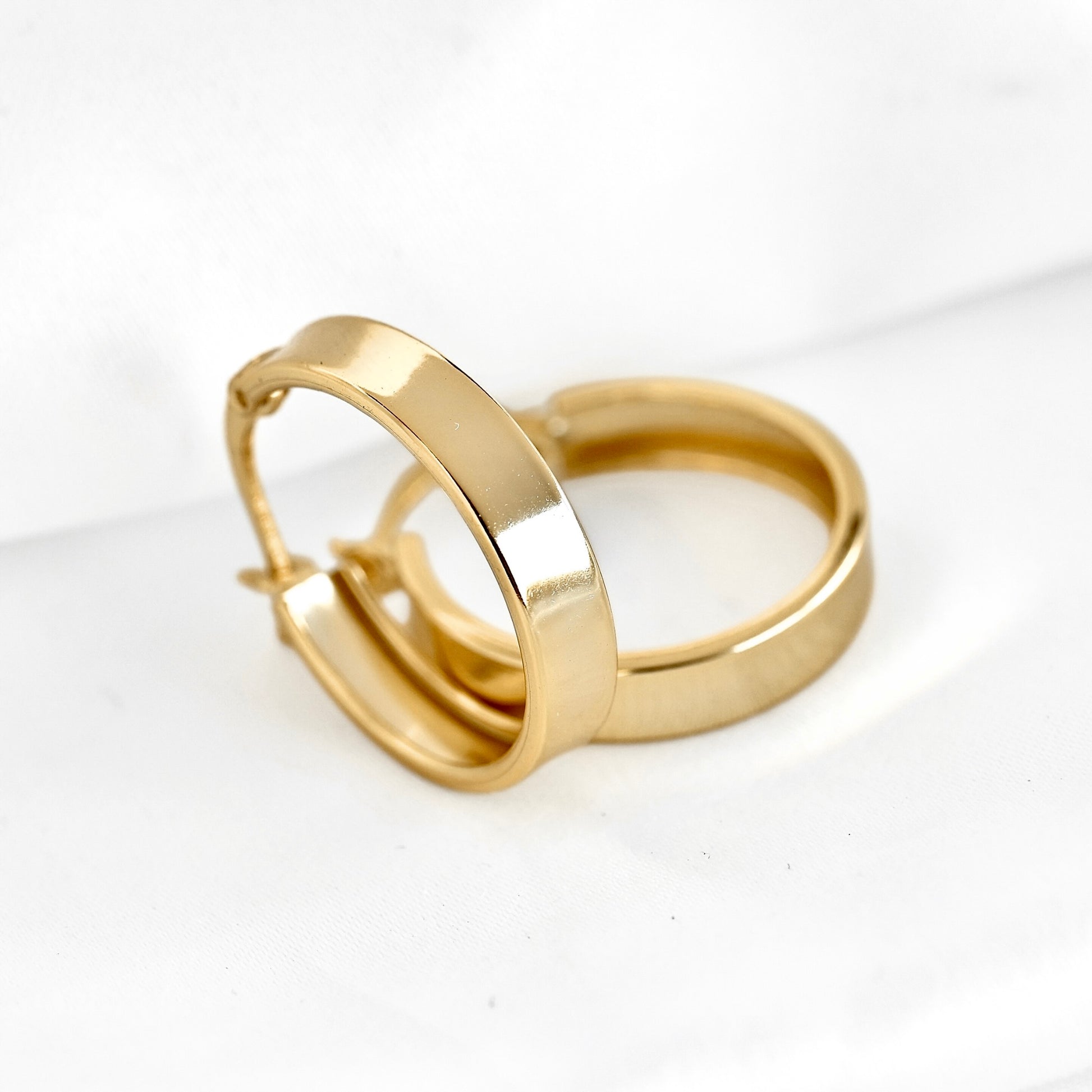 A pair of wide gold hoop earrings with a polished finish, displayed on a clean white background.