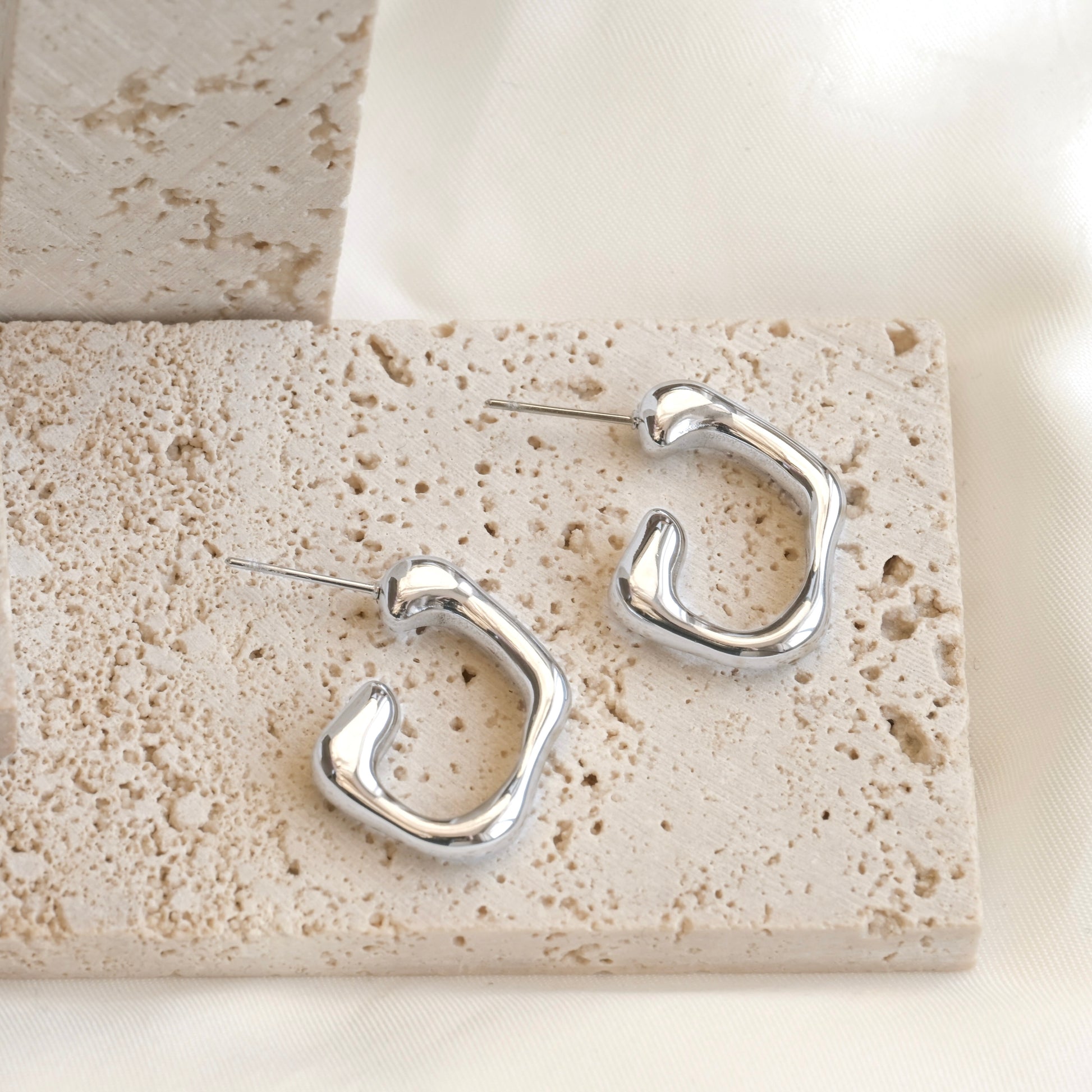 Silver molten hoop earrings on a textured stone surface