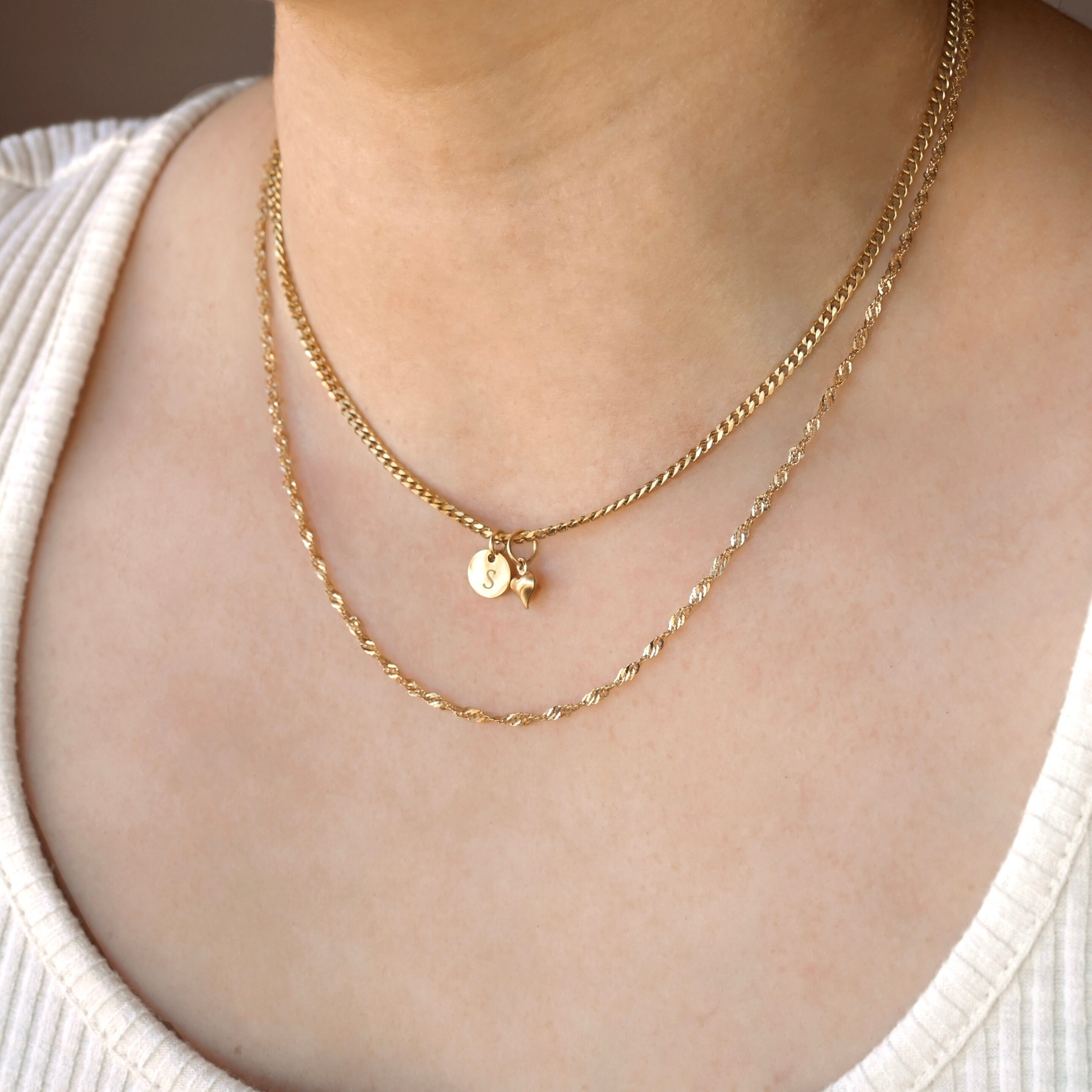 20" Gold twisted chain layered with a dainty curb chain with two small pendants on a person wearing a white top.