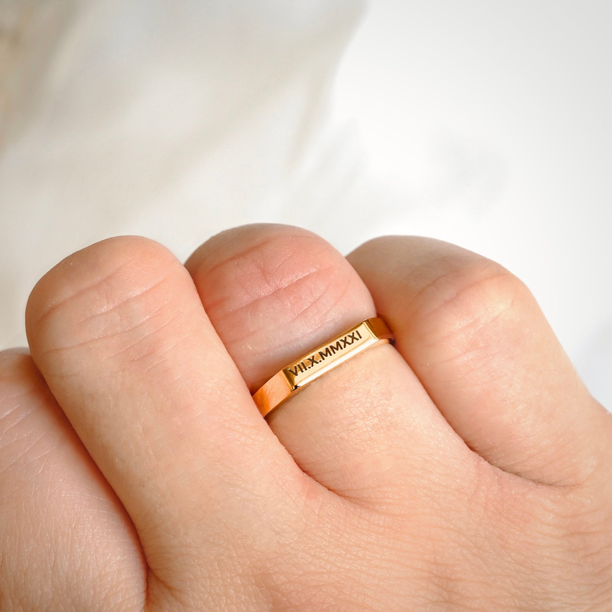 Gold ring with engraved numerals on a finger against a white background