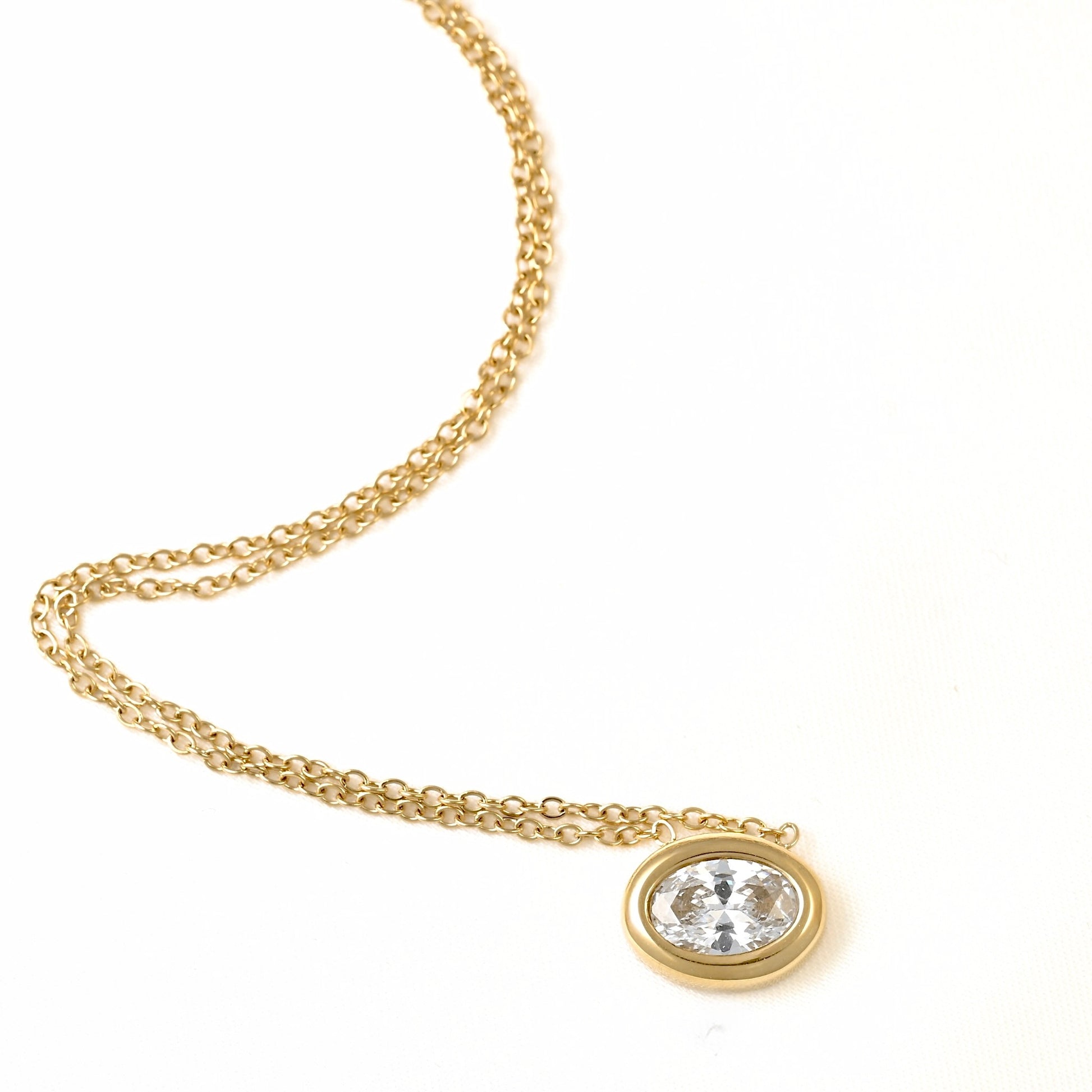 A gold chain necklace with an oval bezel setting holding a clear faceted gemstone, photographed on a plain white background.
