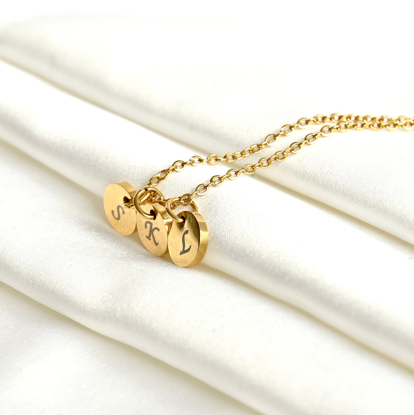 Gold necklace with three round  letter discs on a white fabric background