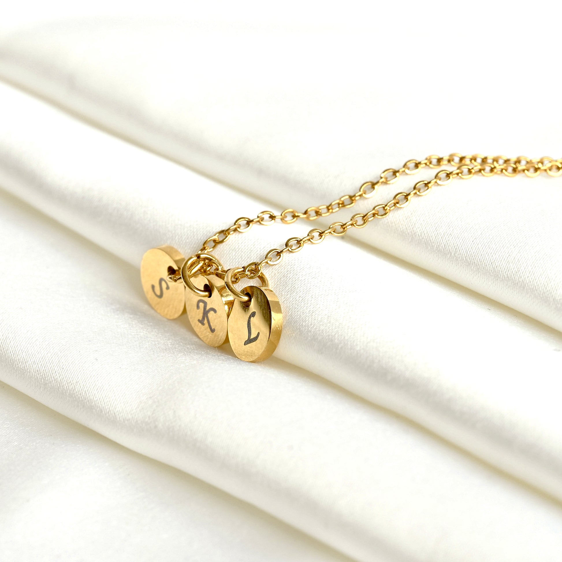 Gold necklace with three round  letter discs on a white fabric background