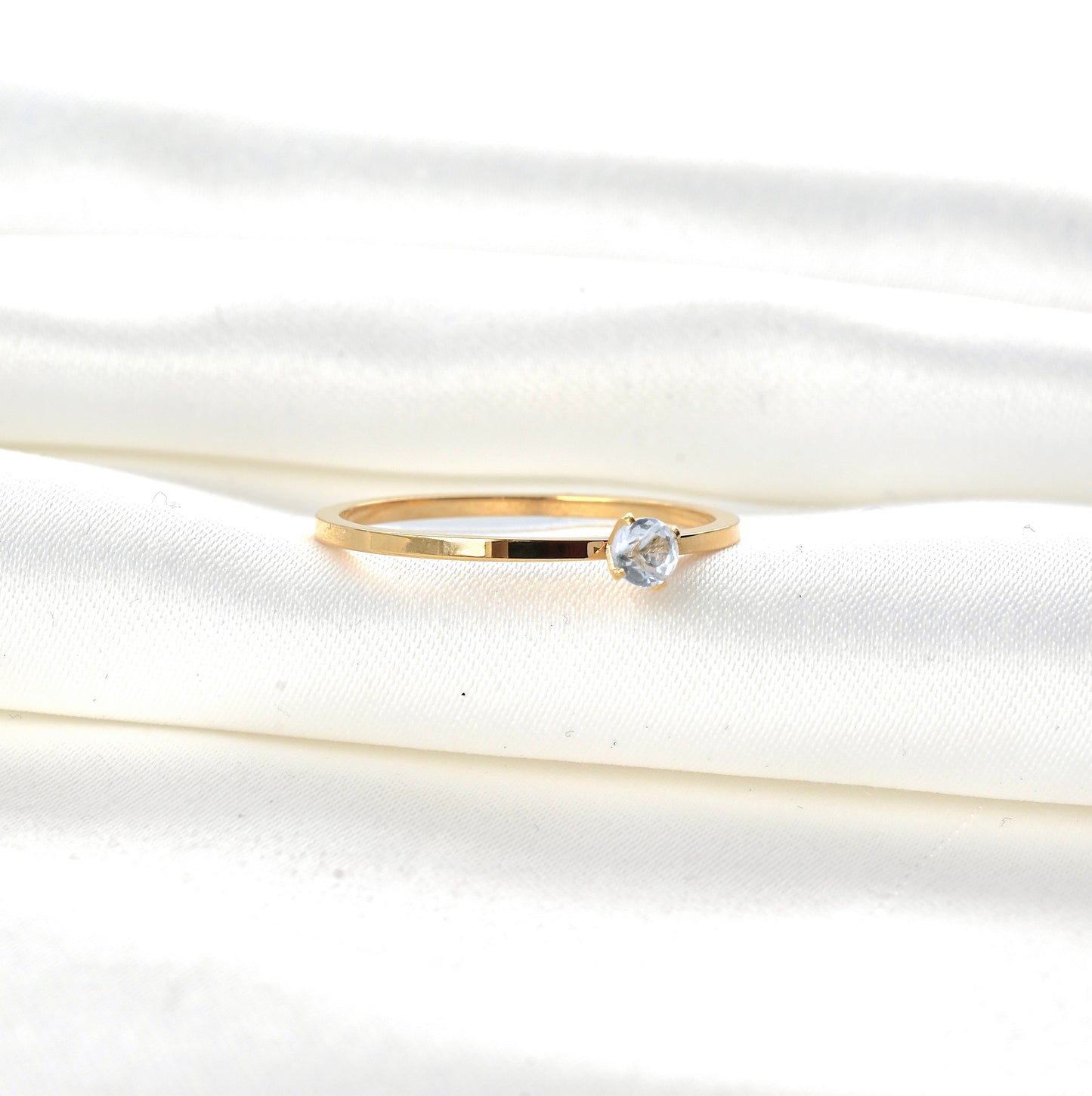 Gold ring with a single diamond on a white satin background