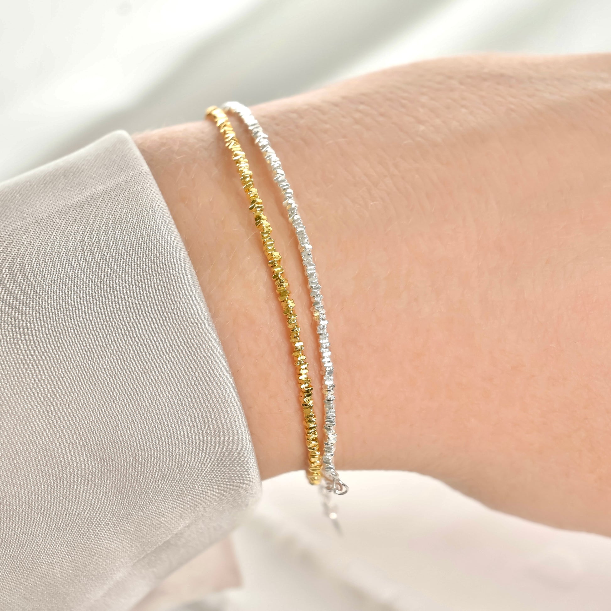 Two gold and silver small beaded bracelets on a wrist against a neutral background