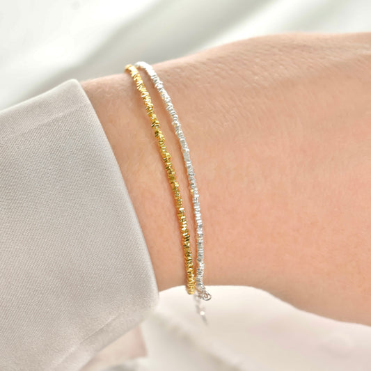 Two gold and silver small beaded bracelets on a wrist against a neutral background