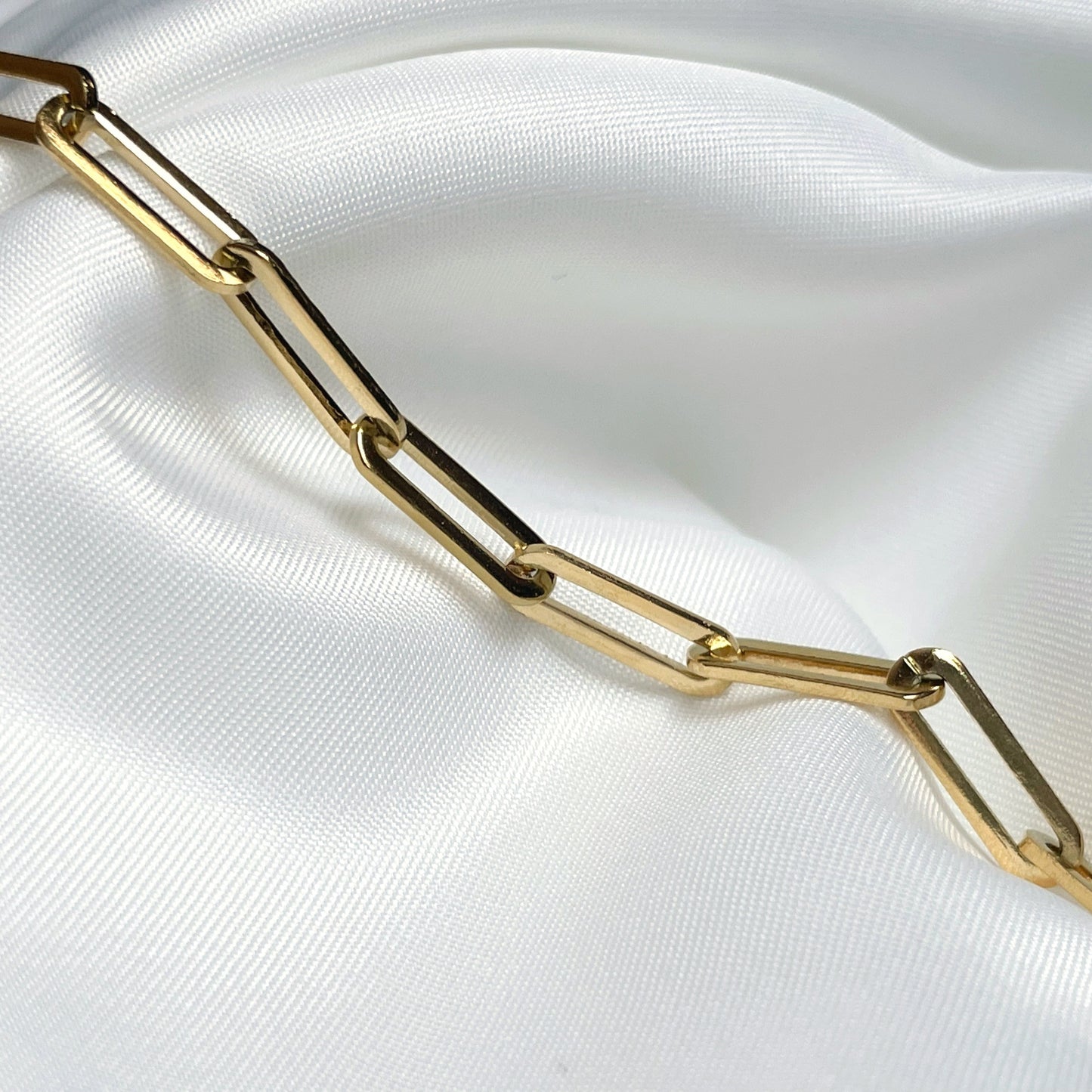 Close-up view of chunky gold paperclip links on a white fabric background