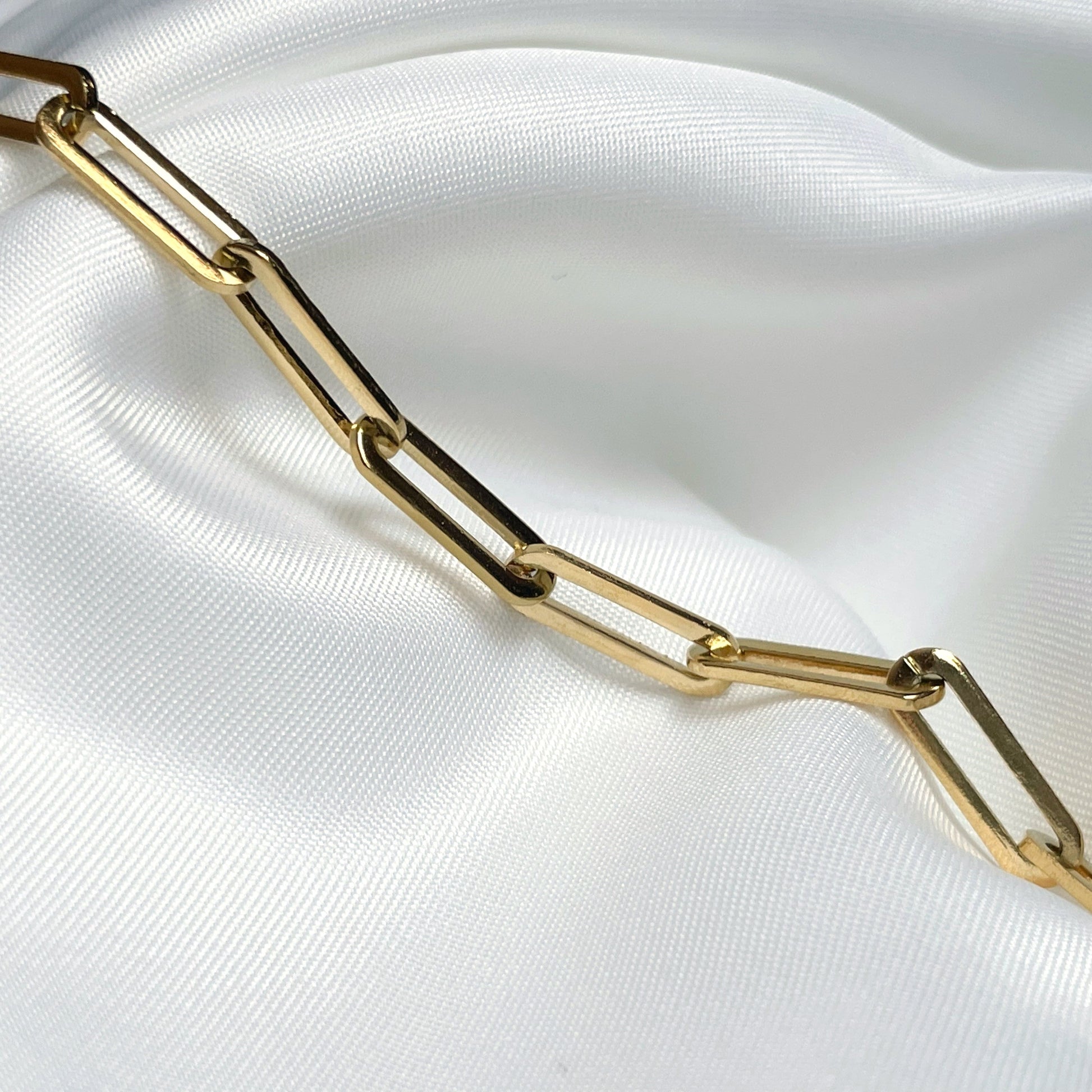 Close-up view of chunky gold paperclip links on a white fabric background
