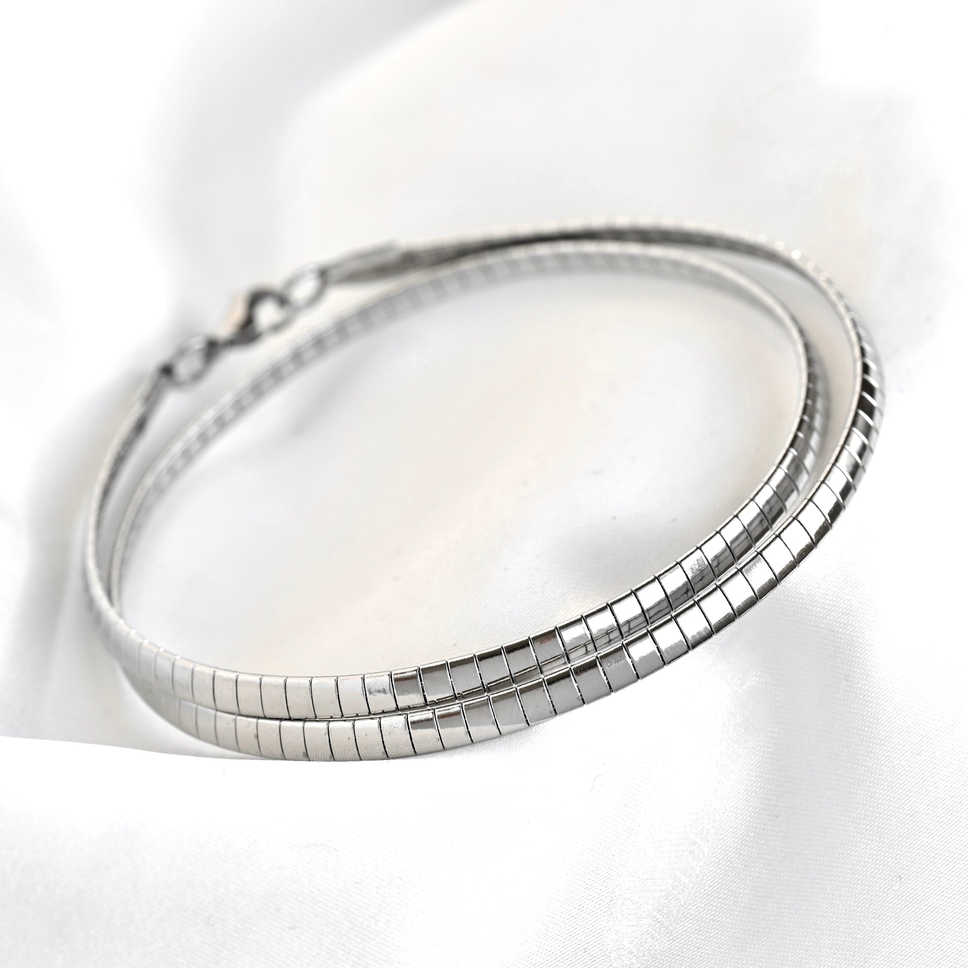 A silver snake chain necklace with a lobster clasp, displayed on a soft white fabric background.