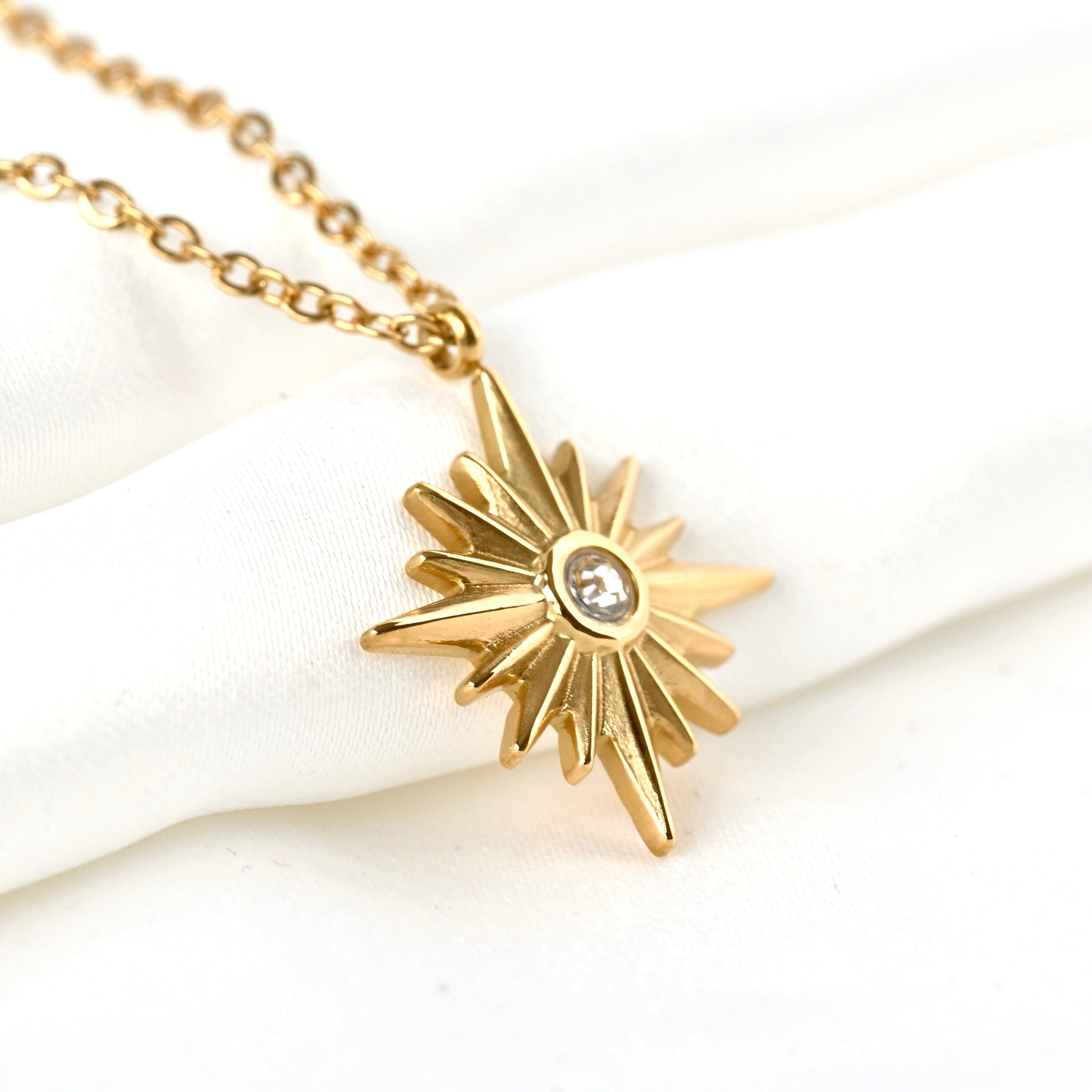 Gold starburst pendant necklace with a central CZ stone on a white background