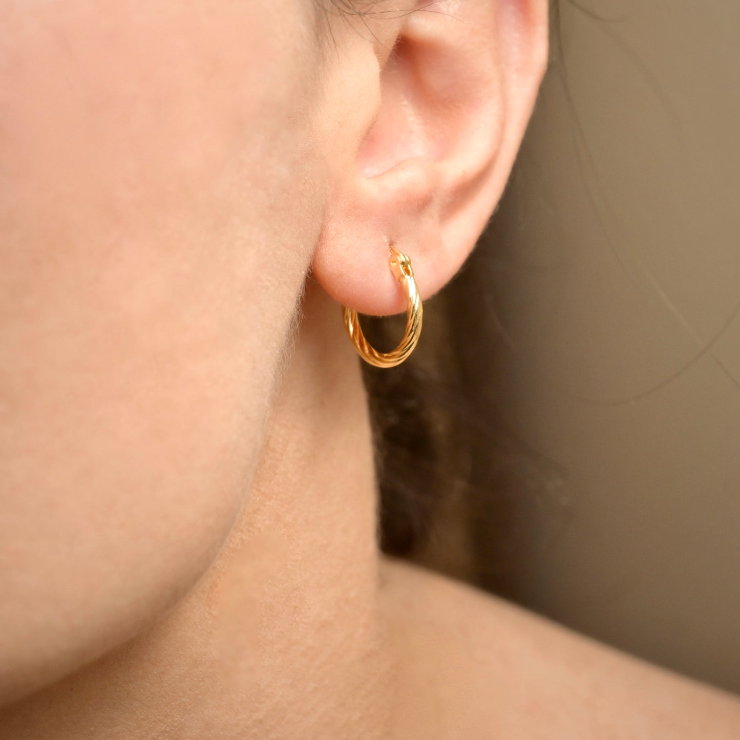 Gold rope hoop earring worn by a person with a neutral background
