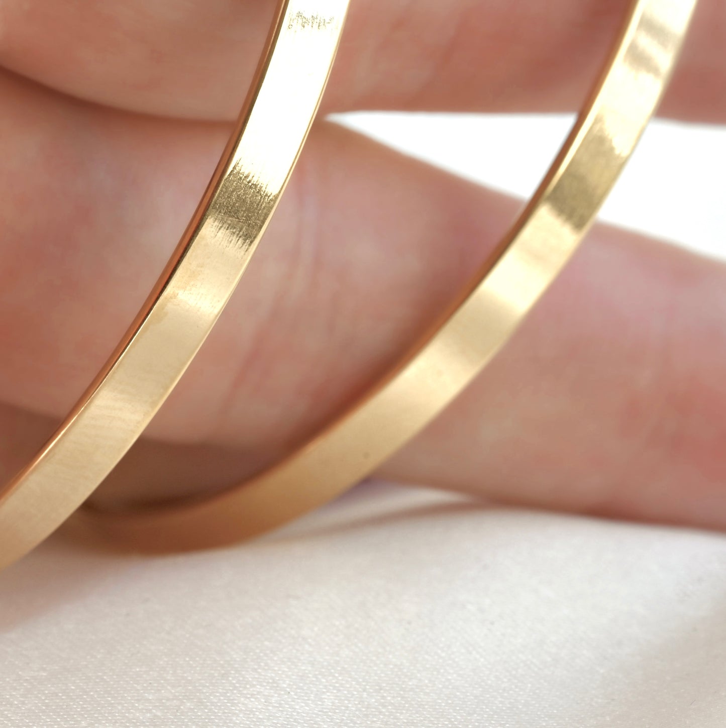 Wide gold angular edge hoops on hand
