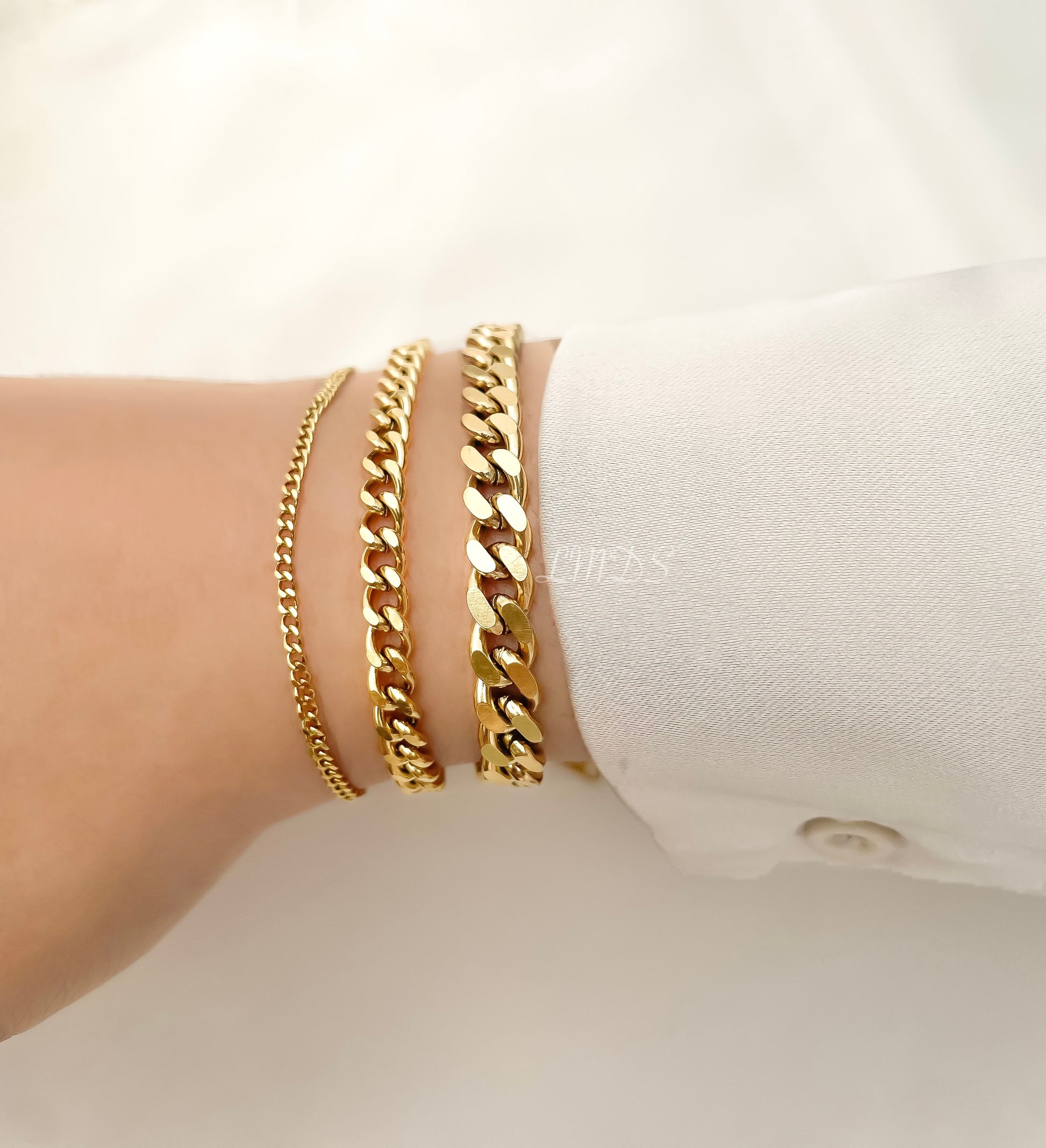 Gold curb chain bracelet stack on a wrist against a white background