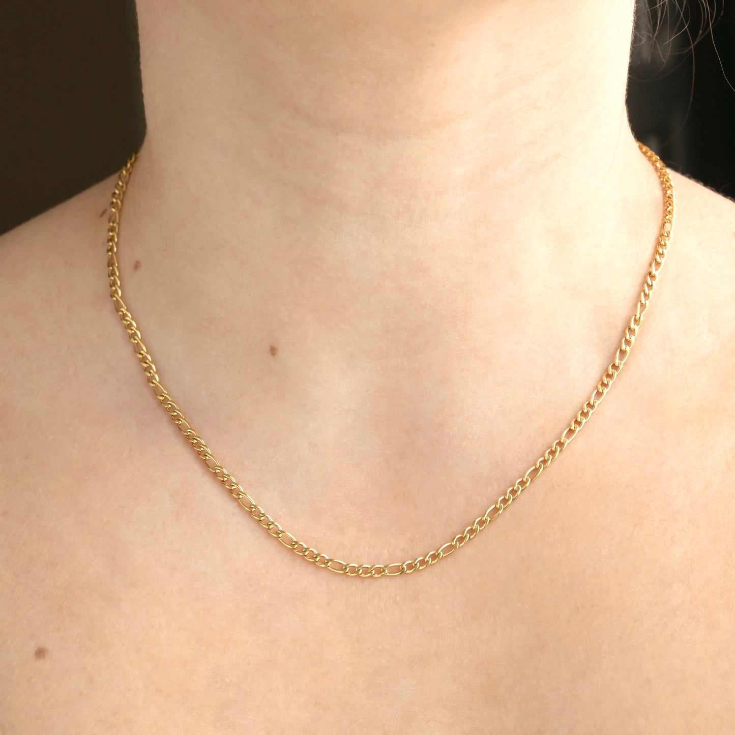 Gold figaro chain on a person's neck: front view