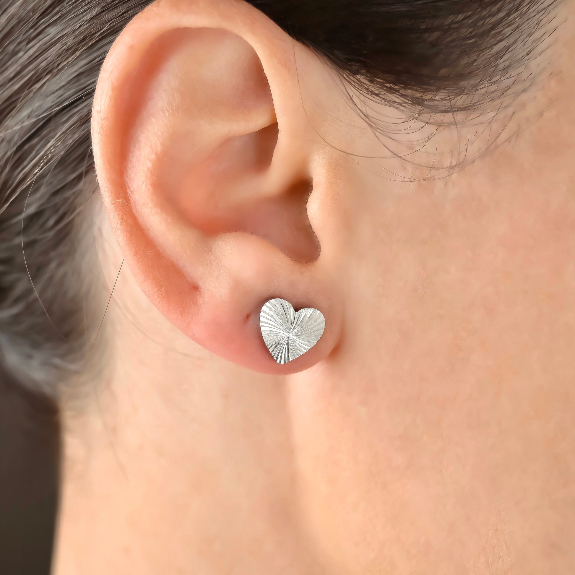 Silver heart-shaped earring worn on a person's ear