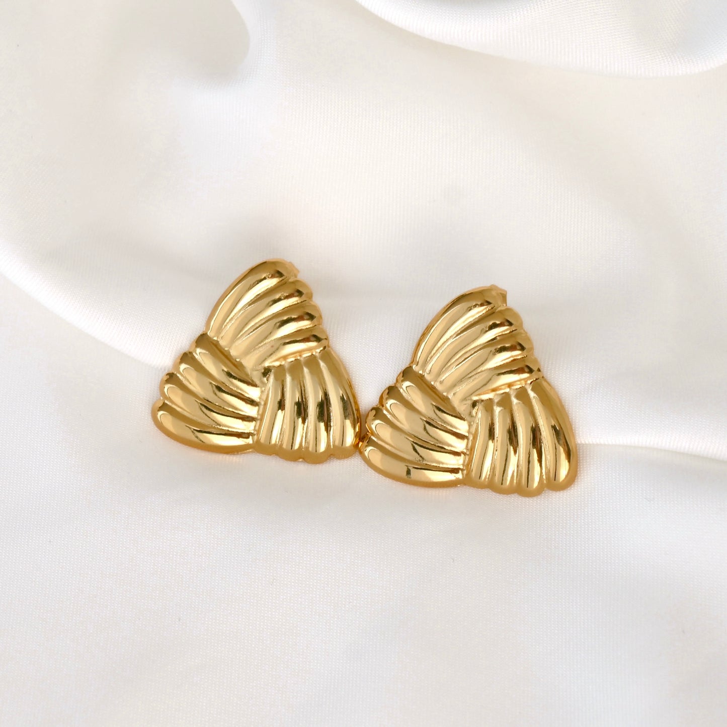 Gold triangle-shaped ribbed earrings on a white fabric