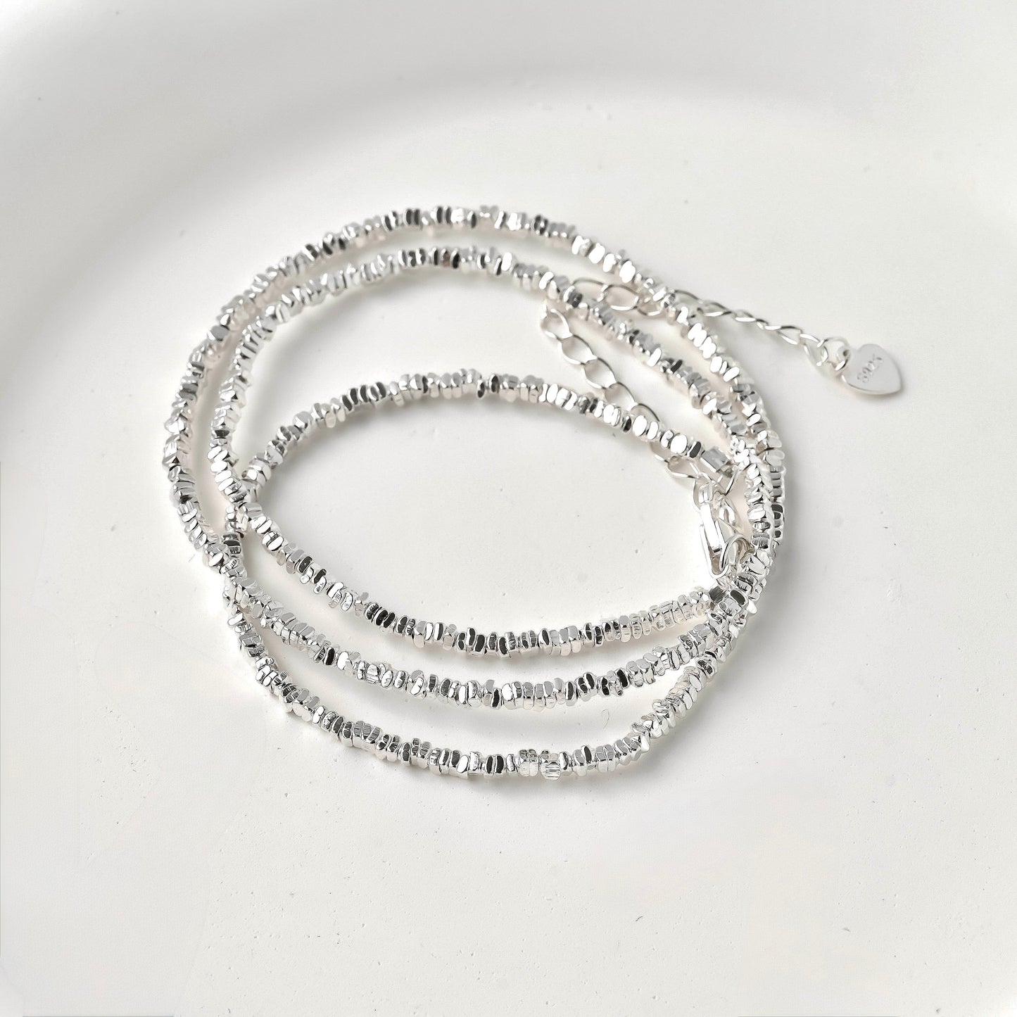 Silver beaded necklace coiled on a light gray background
