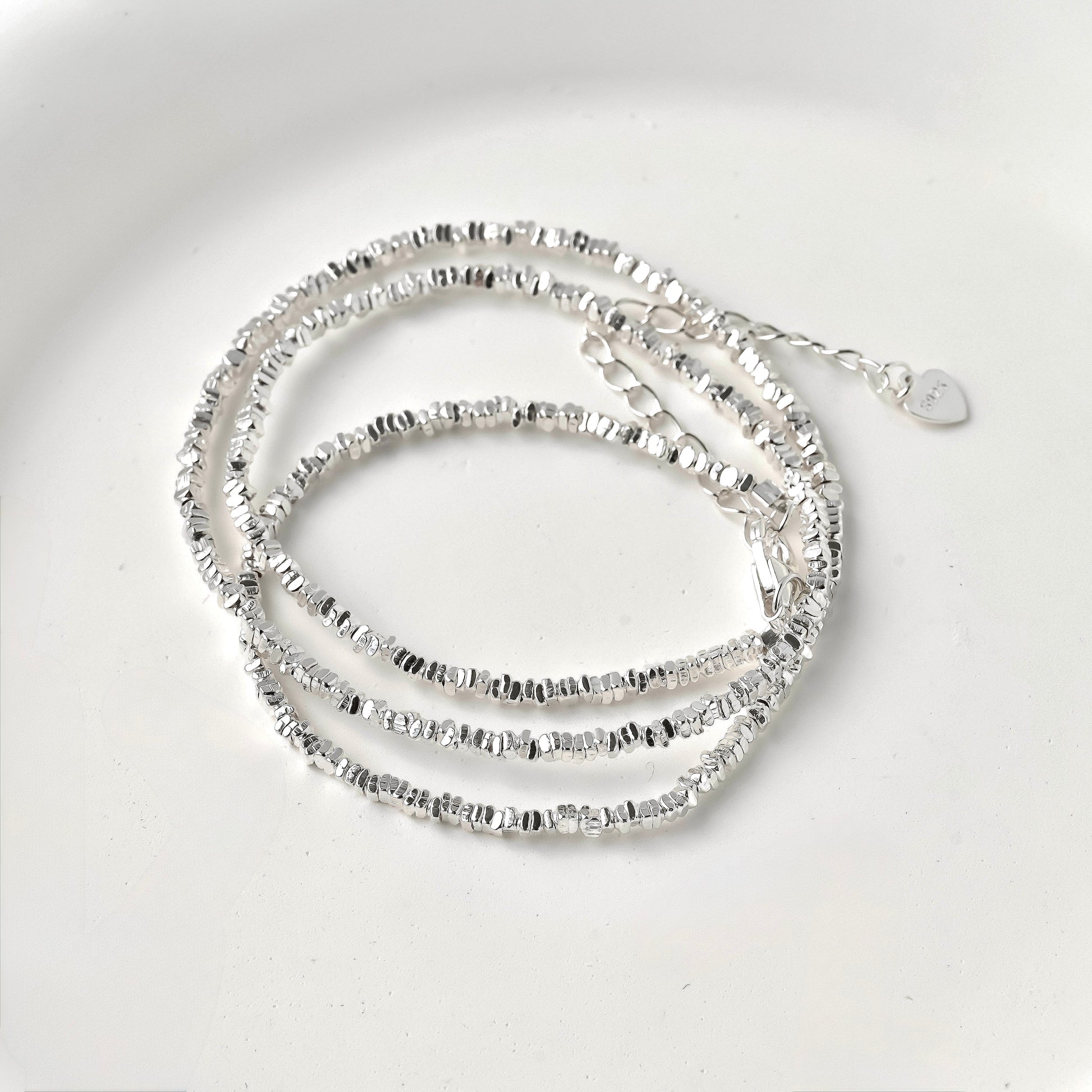 Silver beaded necklace coiled on a light gray background