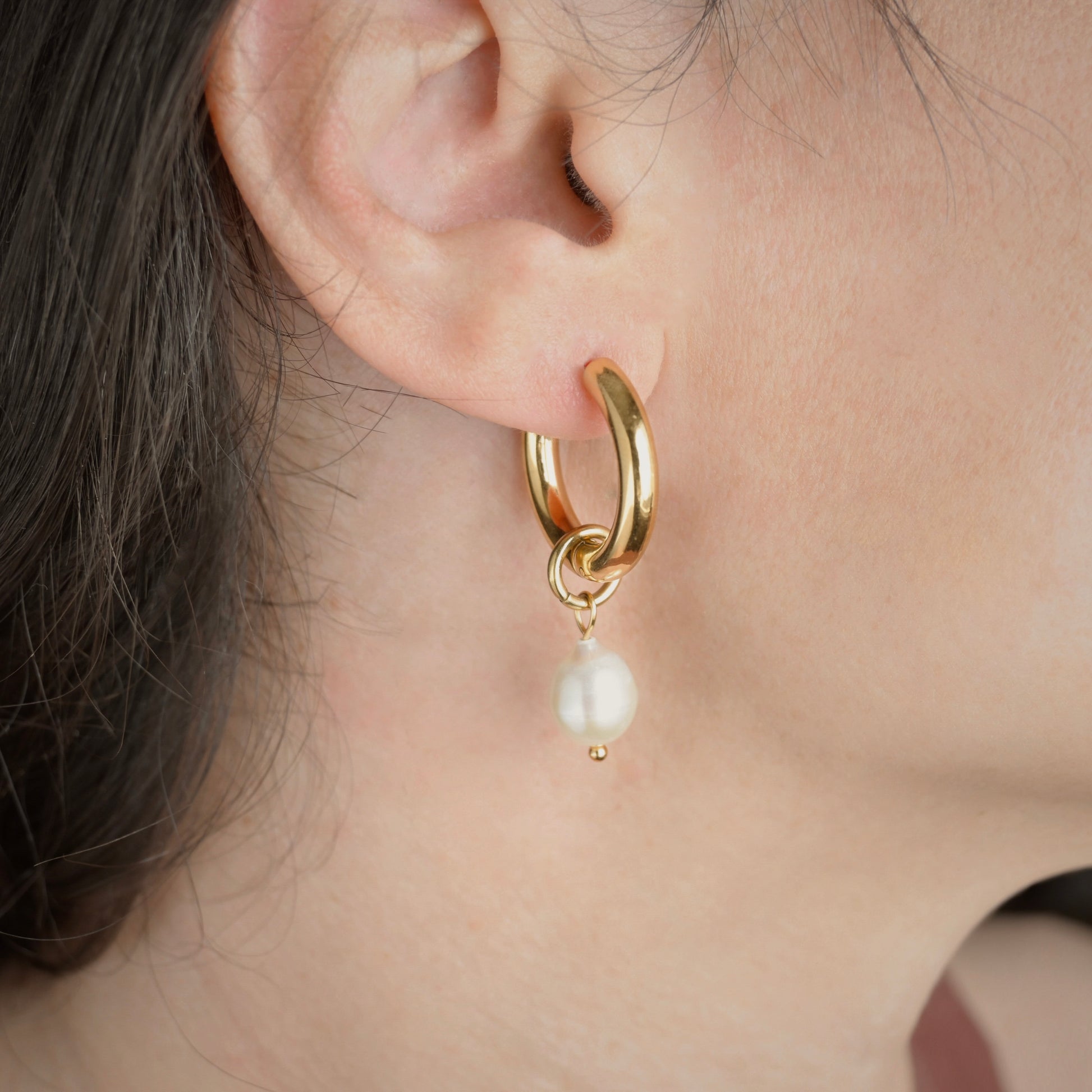 Medium thick gold tunnel hoop earring with a pearl drop charm worn by a person