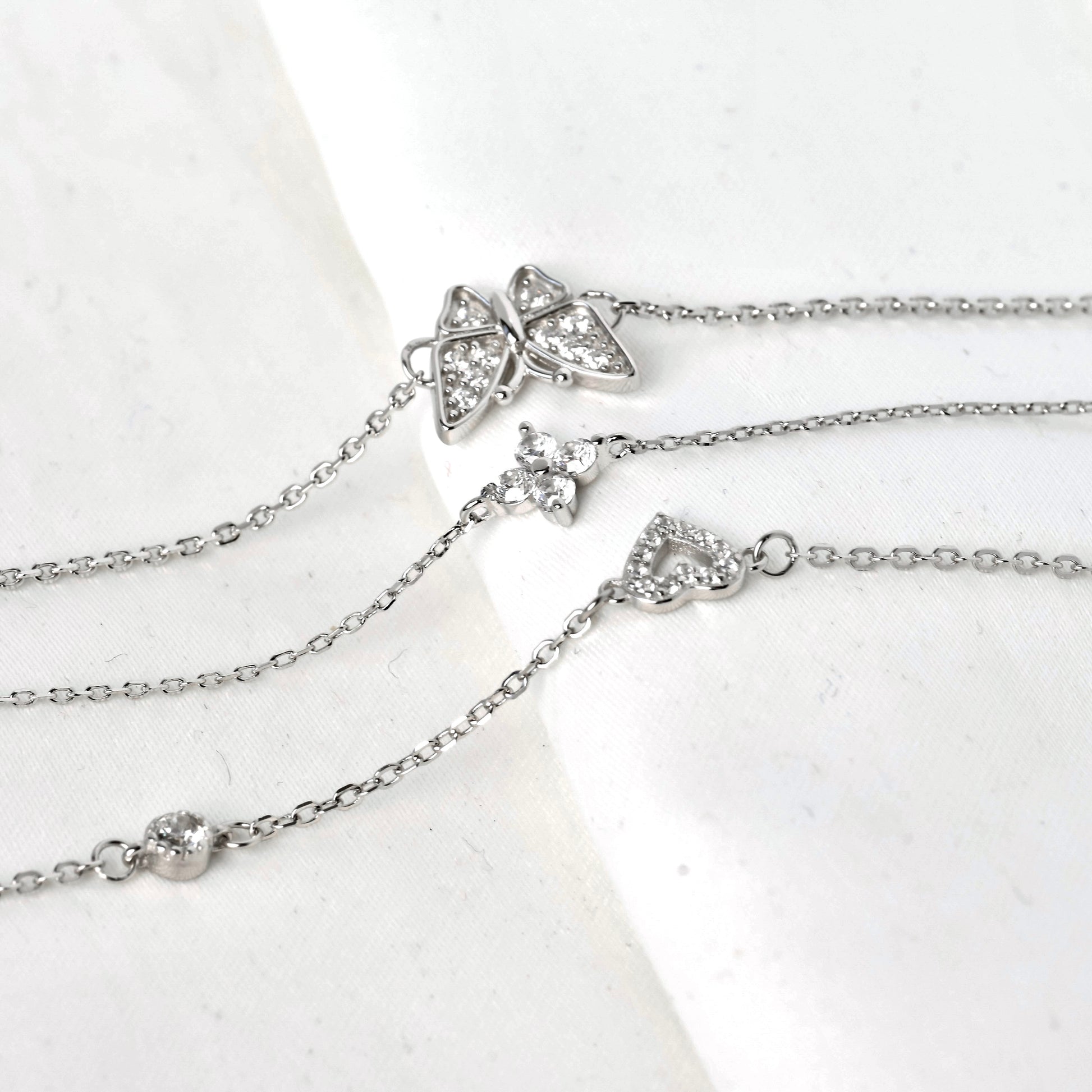 Silver charm bracelets with butterfly clover and heart pendants on a white background