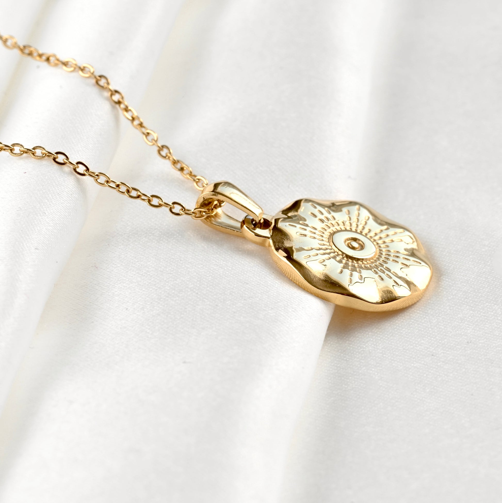 Side view of gold sun medallion necklace on a white background