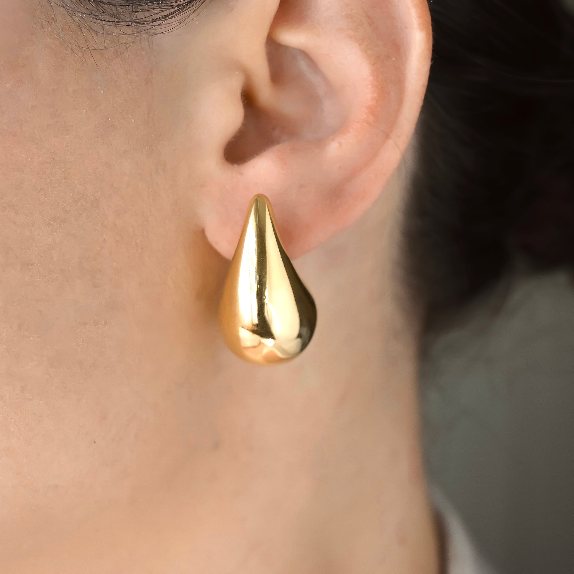 Gold teardrop dome earrings worn on an ear with a blurred background