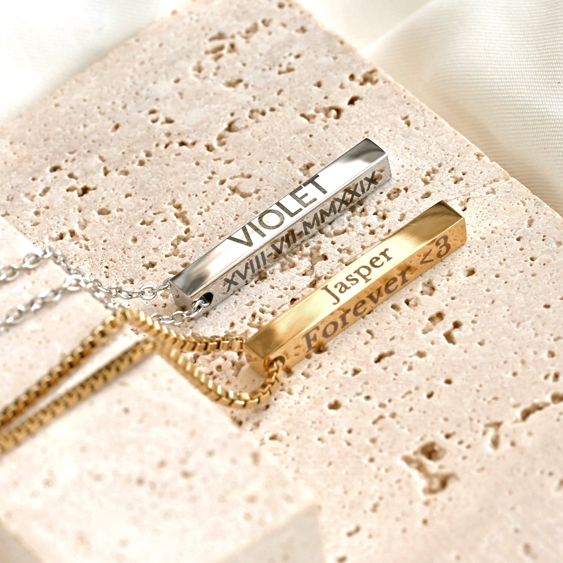 Two gold necklaces with engraved names on a textured beige surface