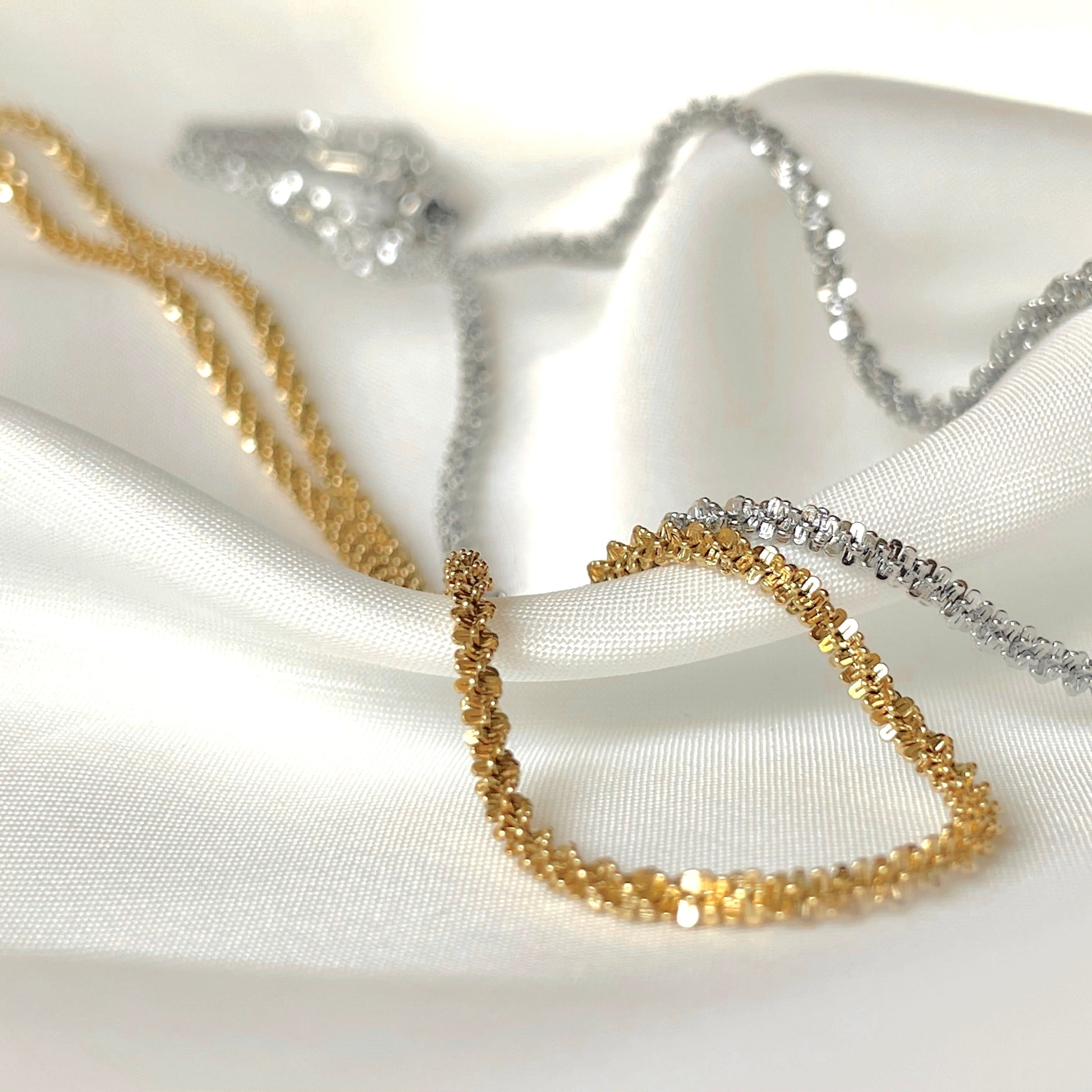 Gold and silver sparkle chain necklaces on a white fabric background