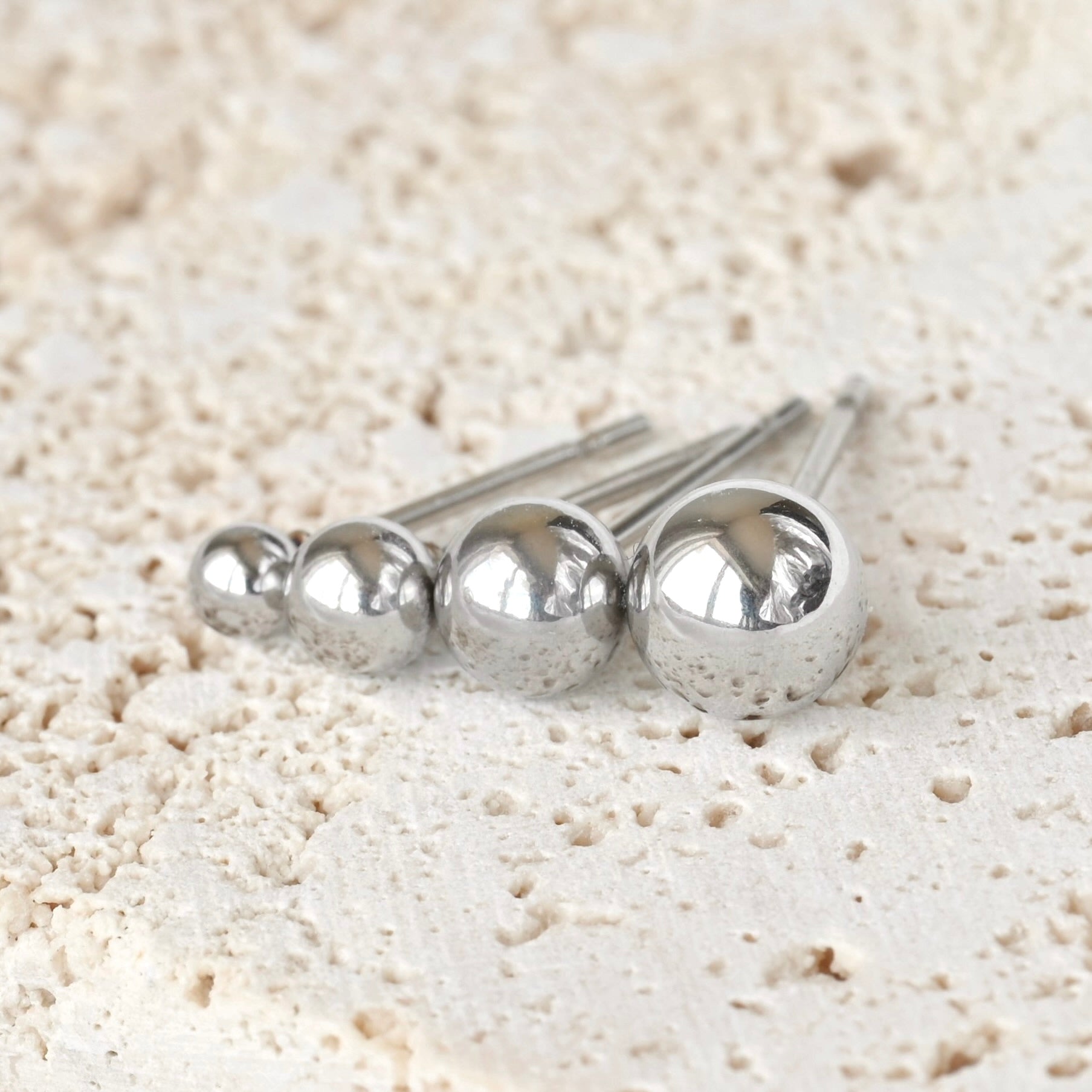 Set of silver metal ball earrings on a textured beige surface