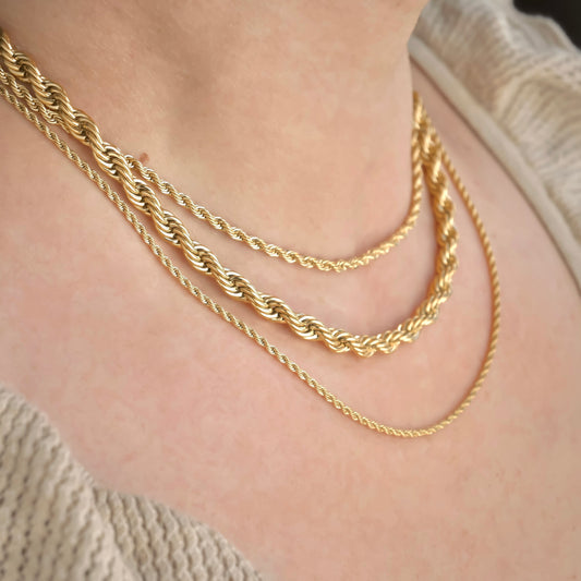 Three gold rope chains in different widths layered on a person's neck with a neutral background