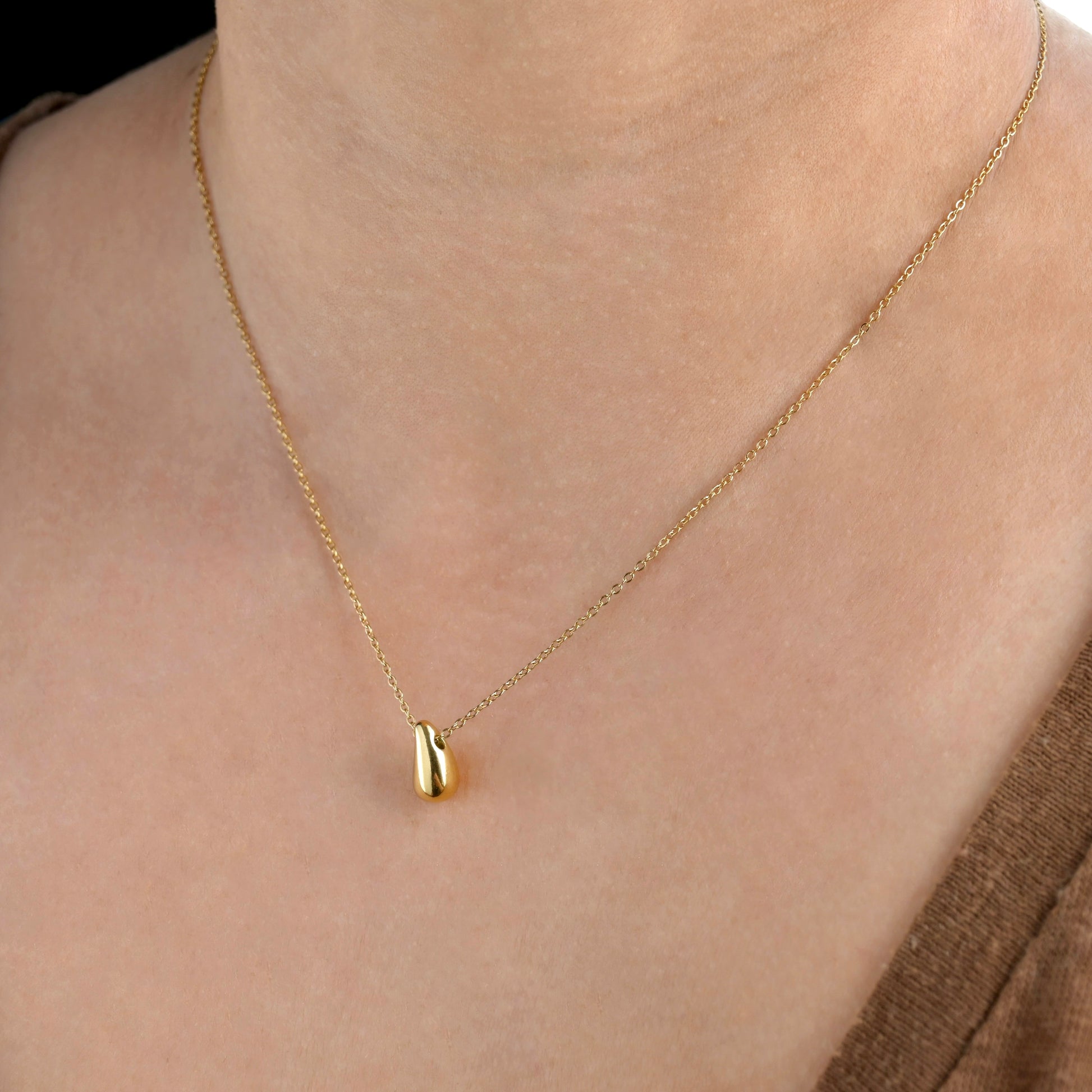 Gold necklace with a small droplet pendant on a person's neck