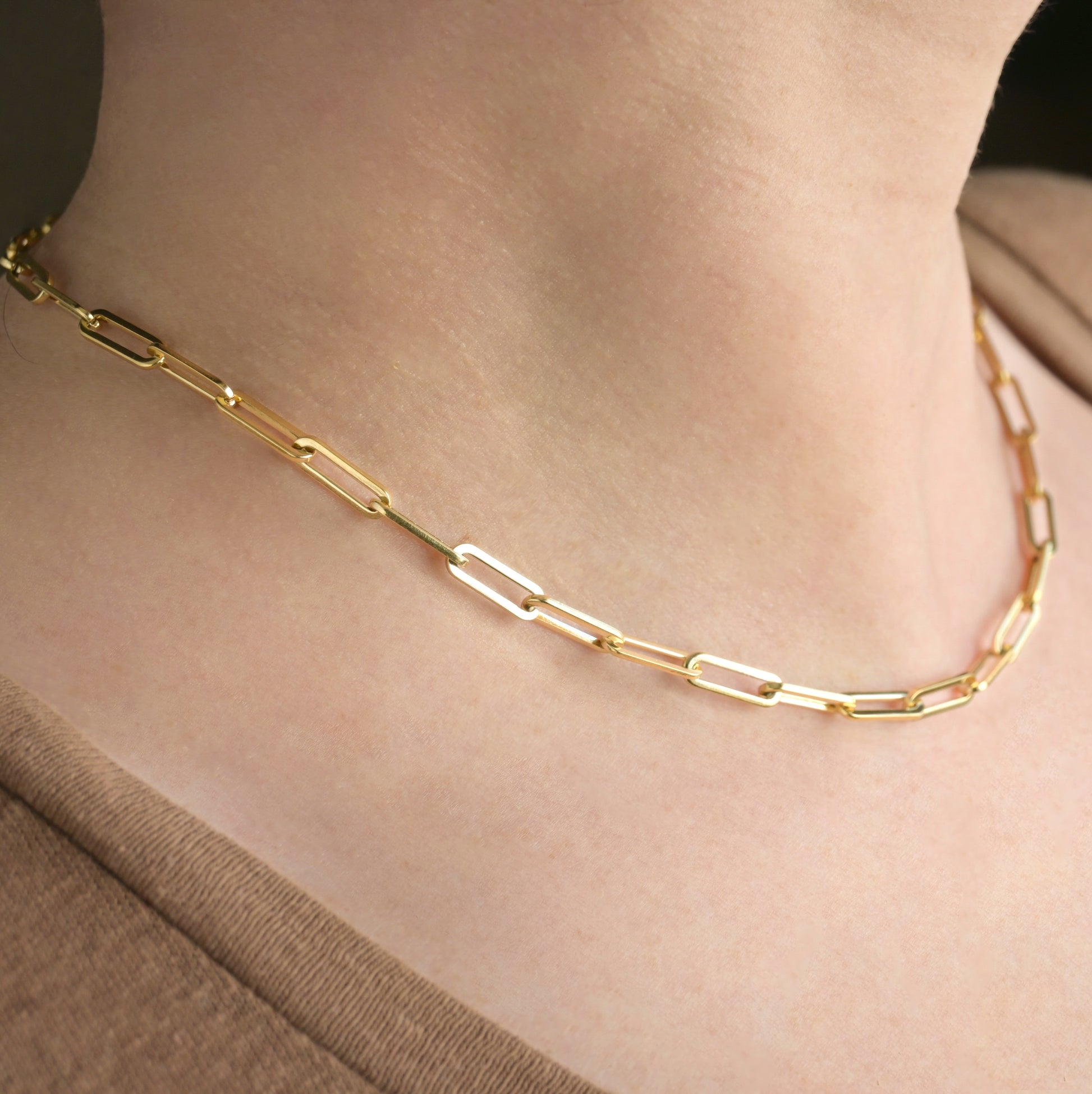 Thick gold  paperclip chain necklace on a person's neck with a neutral background