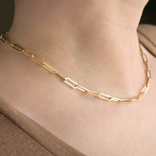 Thick gold  paperclip chain necklace on a person's neck with a neutral background