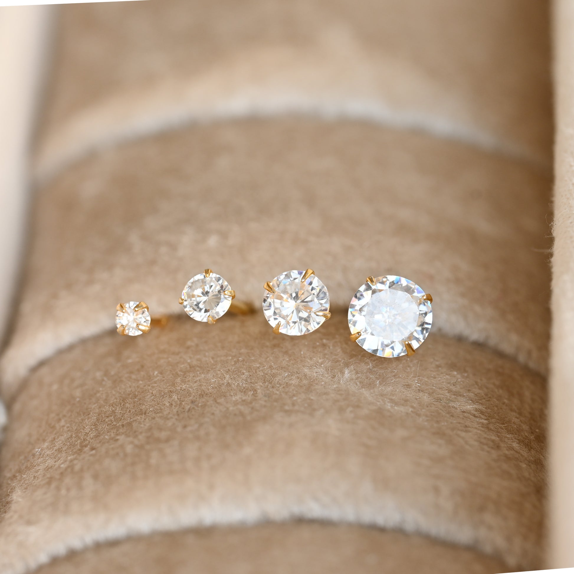 front view of four diamond stud earrings on a beige fabric background
