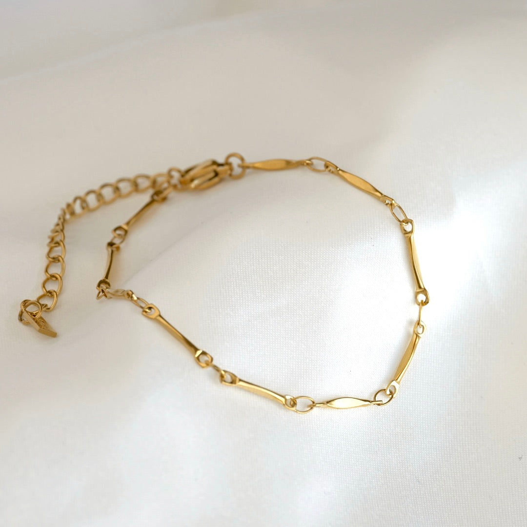 A gold chain bracelet with alternating polished oval links and smaller round links, displayed on a soft white fabric background.