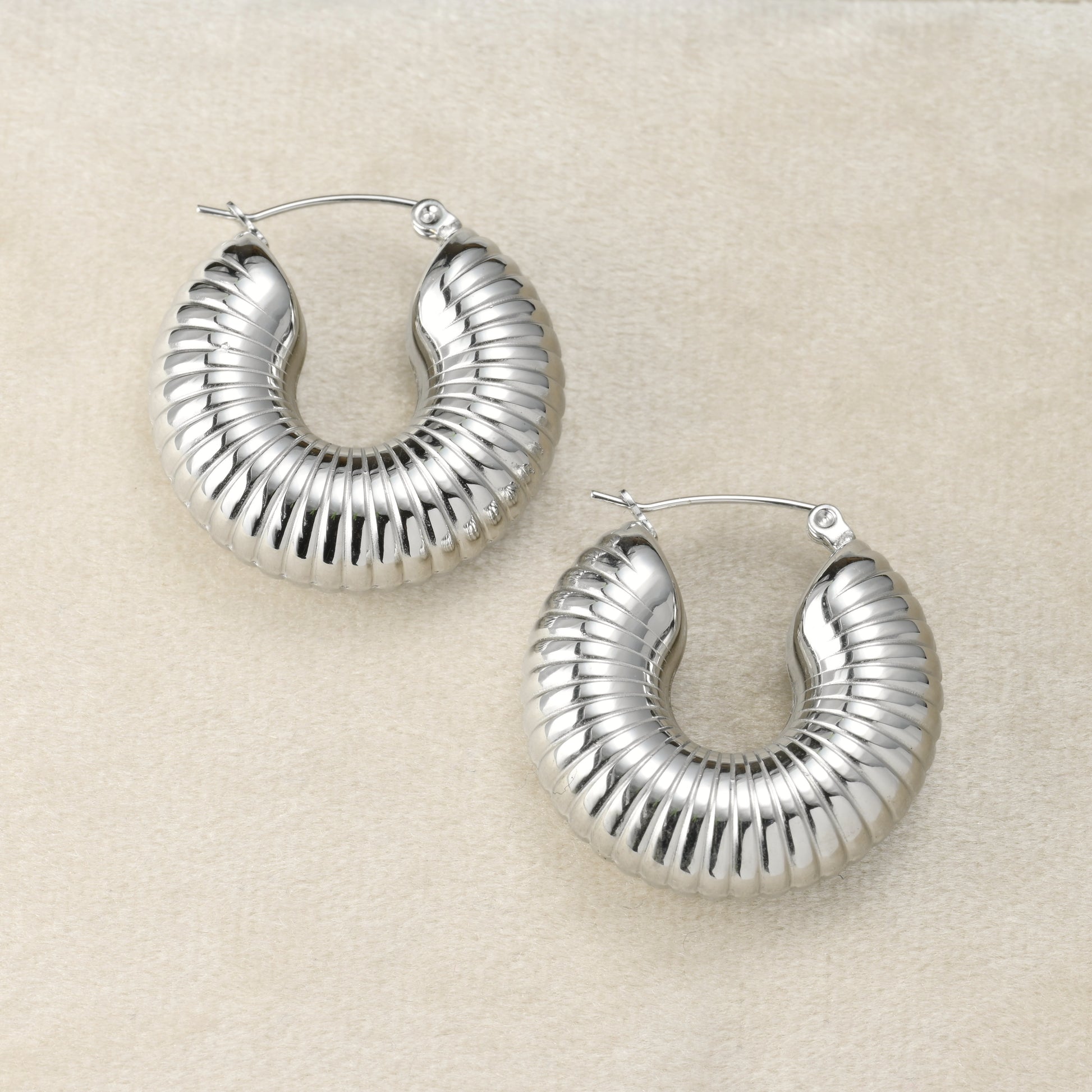 Pair of chunky silver hoops on a beige fabric background