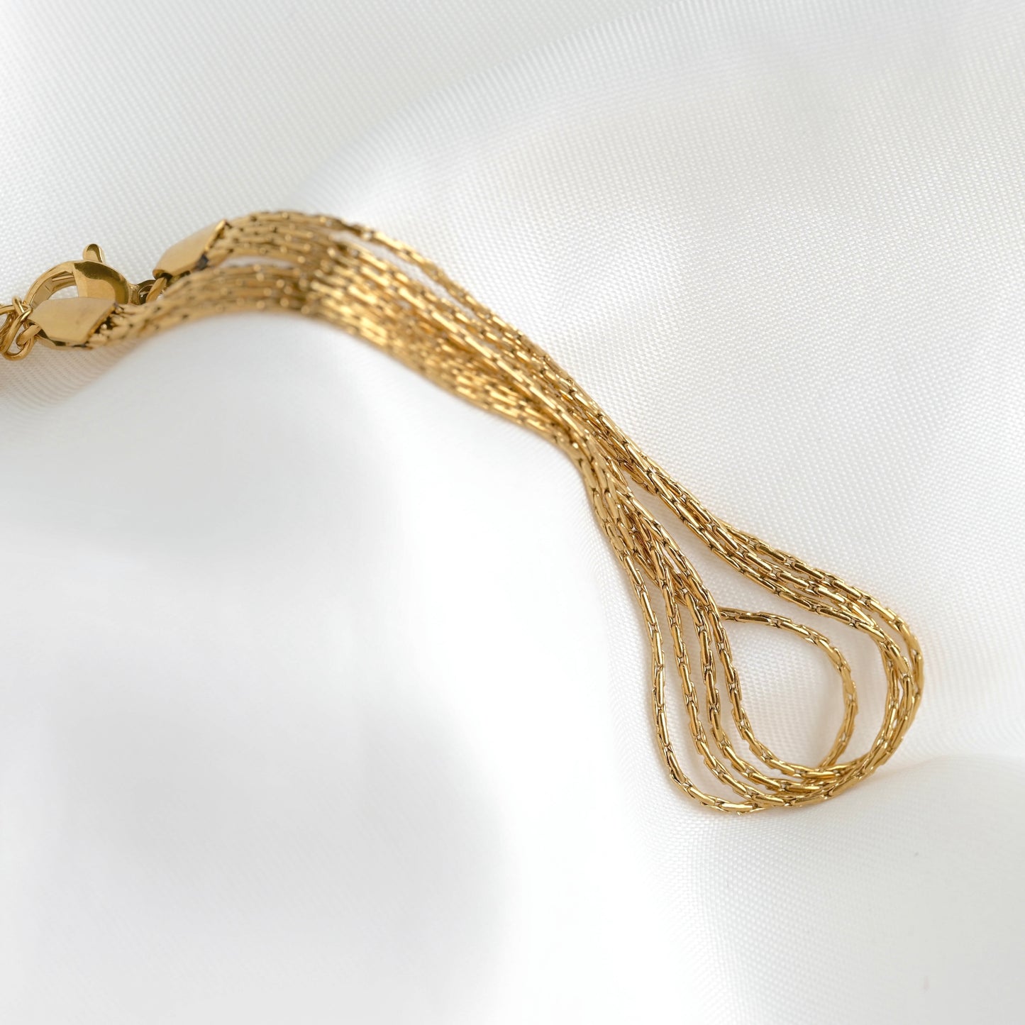 A close-up of a gold chain bracelet with a lobster clasp, resting on a white textured fabric background.