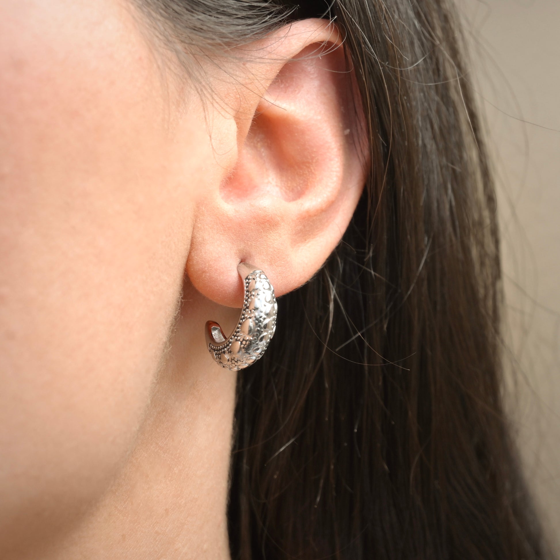 Close-up of an ear wearing a silver hoop earring with a beige background