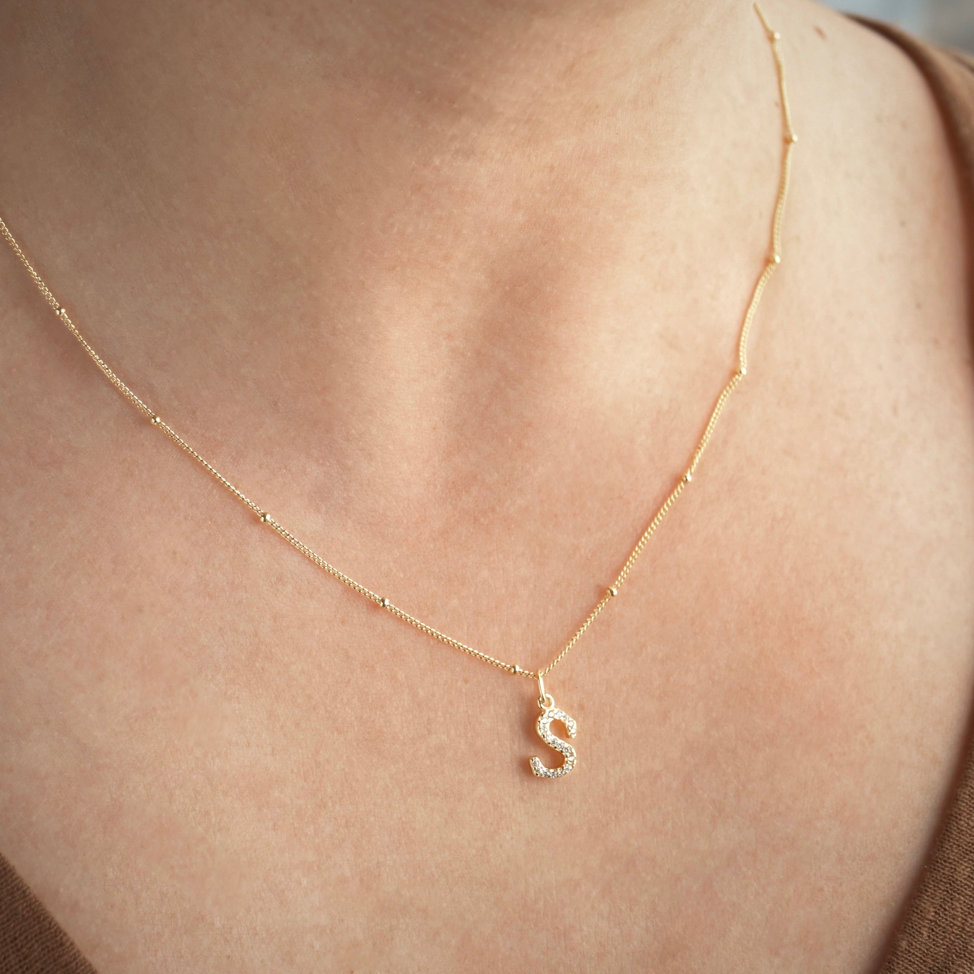 Gold beaded chain necklace with a diamond 'S' pendant on a person's neck