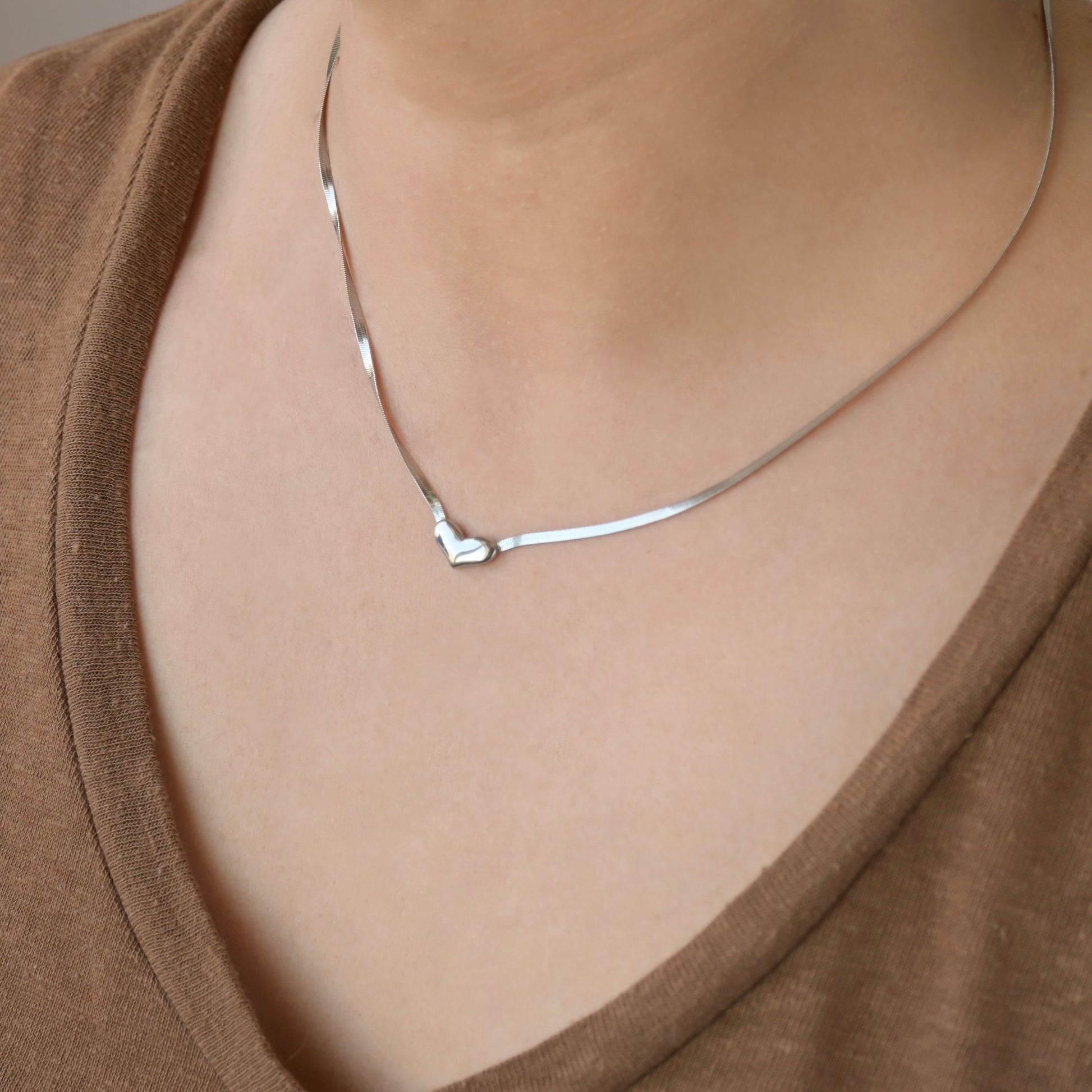 Silver heart necklace on a person wearing a brown top