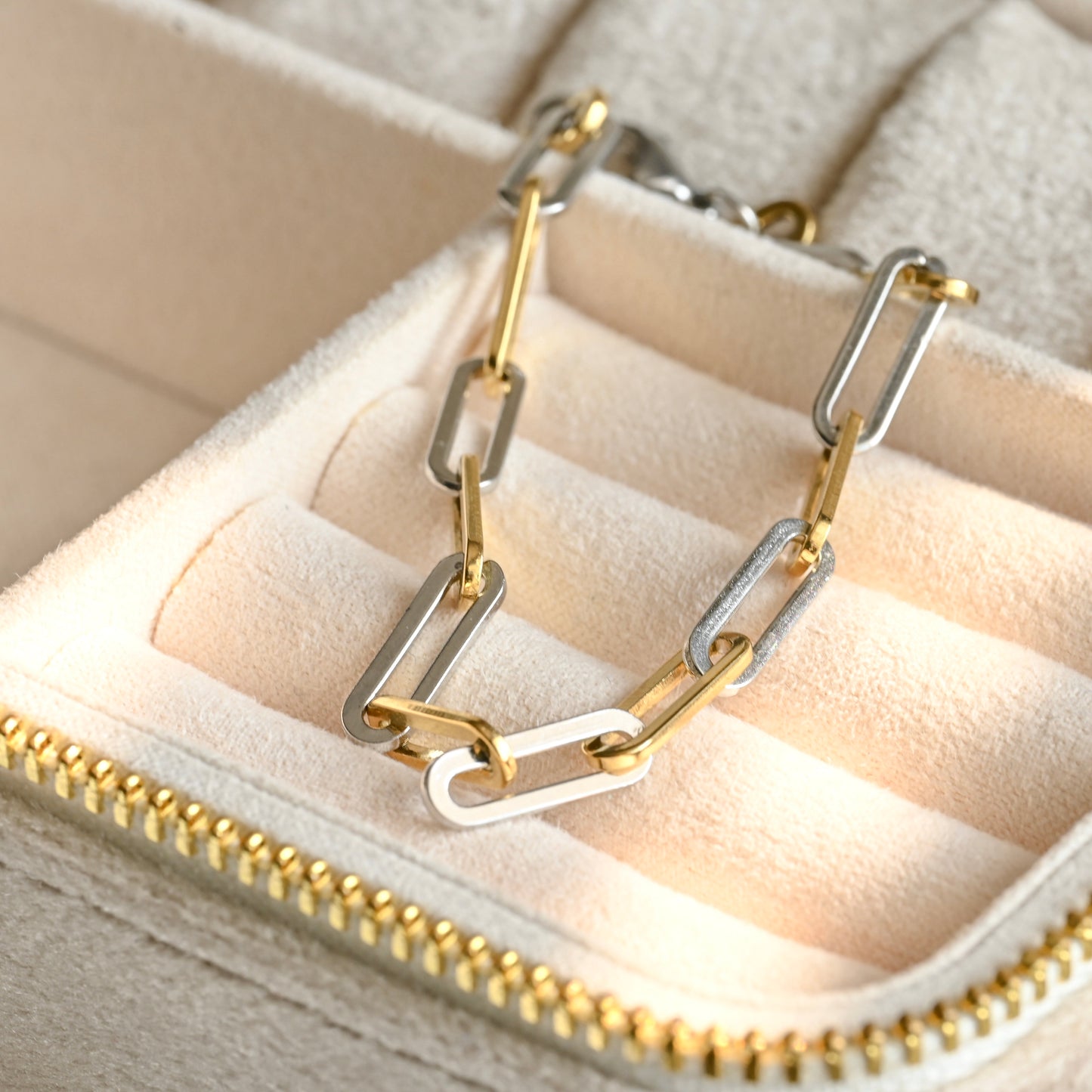 Gold and silver chain-link bracelet on a beige jewelry box