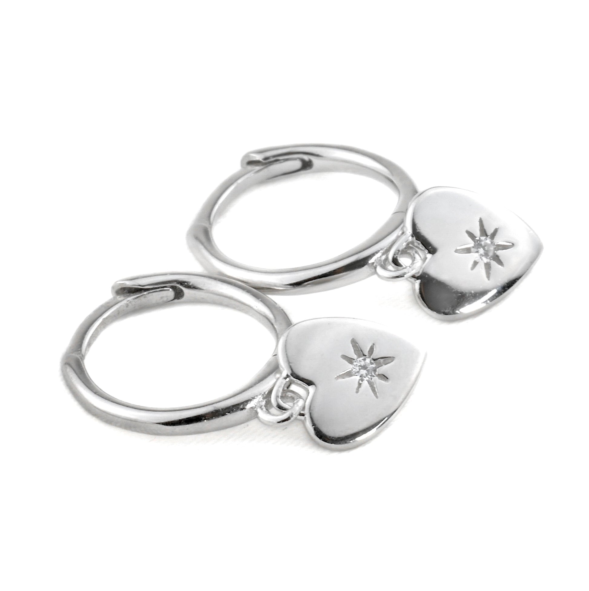Pair of silver hoop earrings with heart-shaped charms with a star-set CZ in the center on a white background