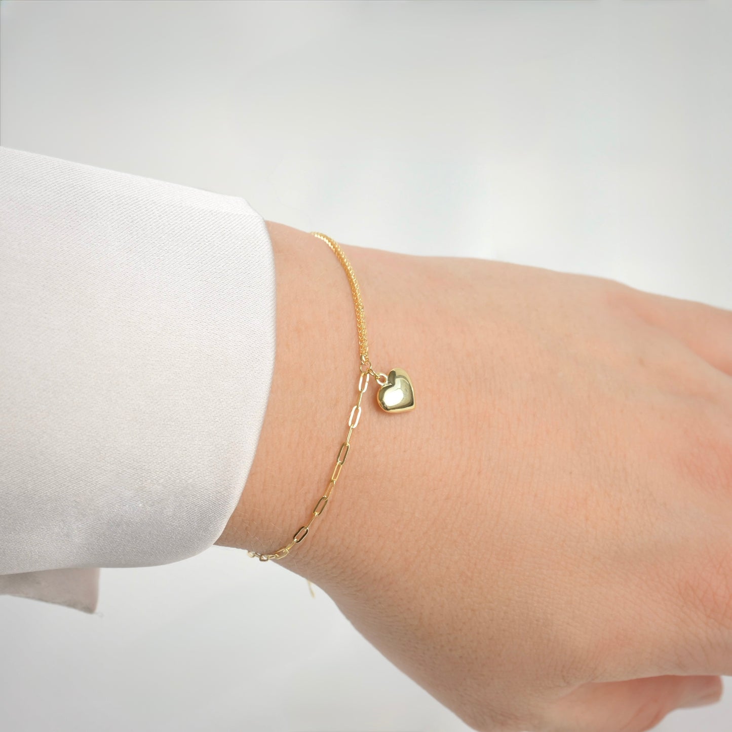 Gold bracelet with a heart-shaped charm on a wrist against a white background