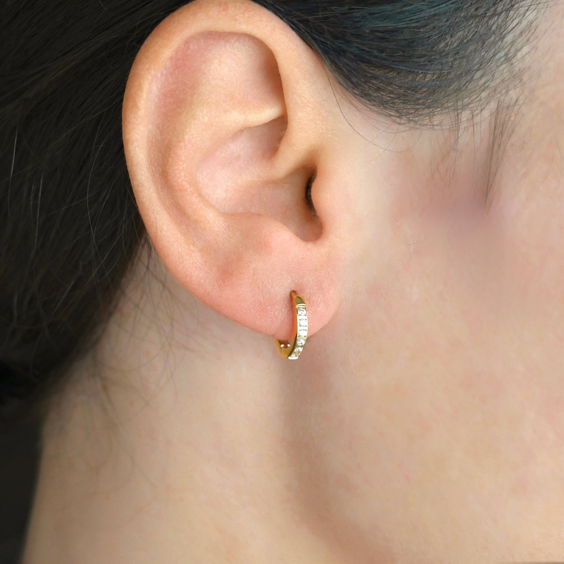 Close-up of an ear wearing a pave cz gold huggie hoop earring with clear stones.