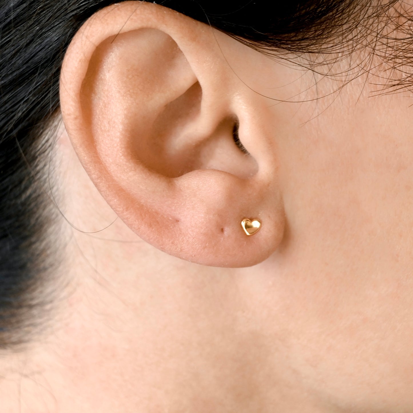 A close-up of a person's ear wearing a small gold heart stud.