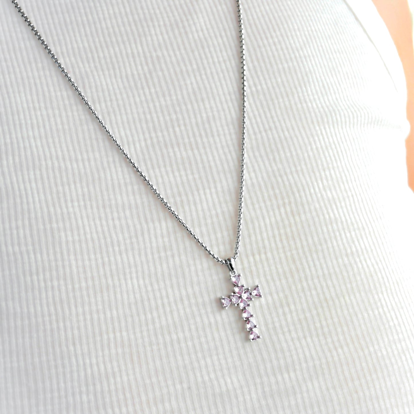 Long silver cross necklace with pink stones on a person wearing ribbed white tank