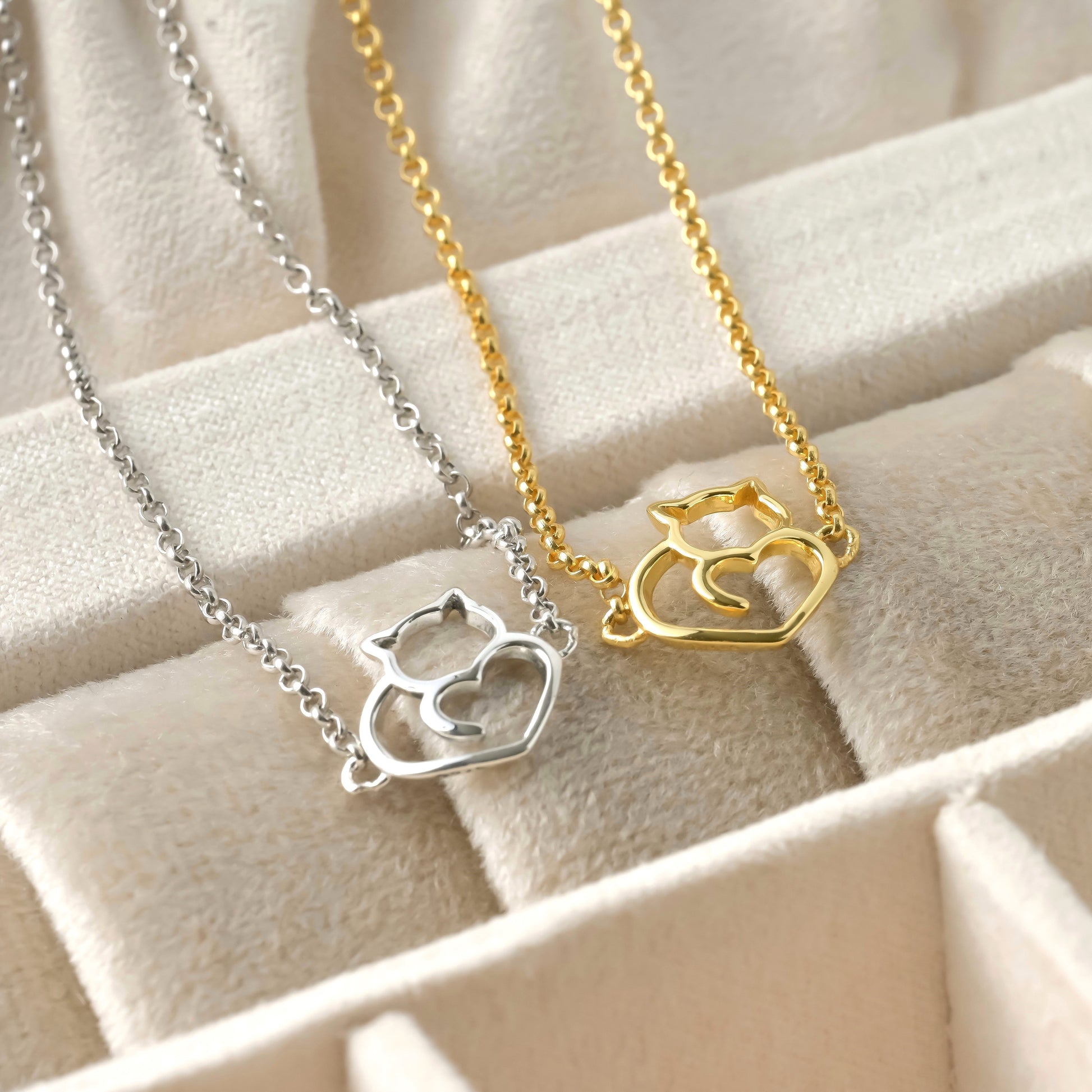 Two cat charm bracelets, one silver and one gold, on a beige fabric background.
