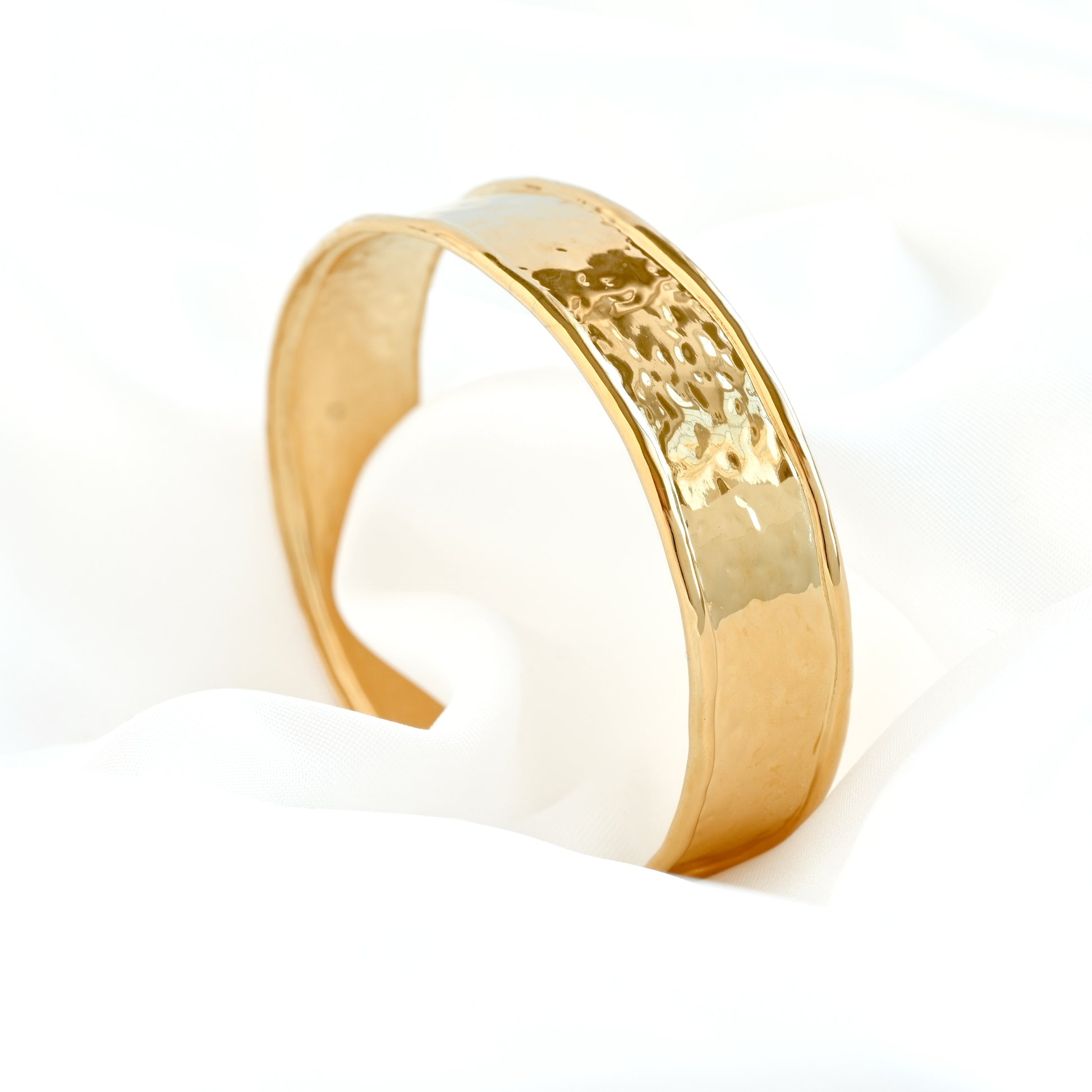 Gold cuff bracelet with a textured design on a white background